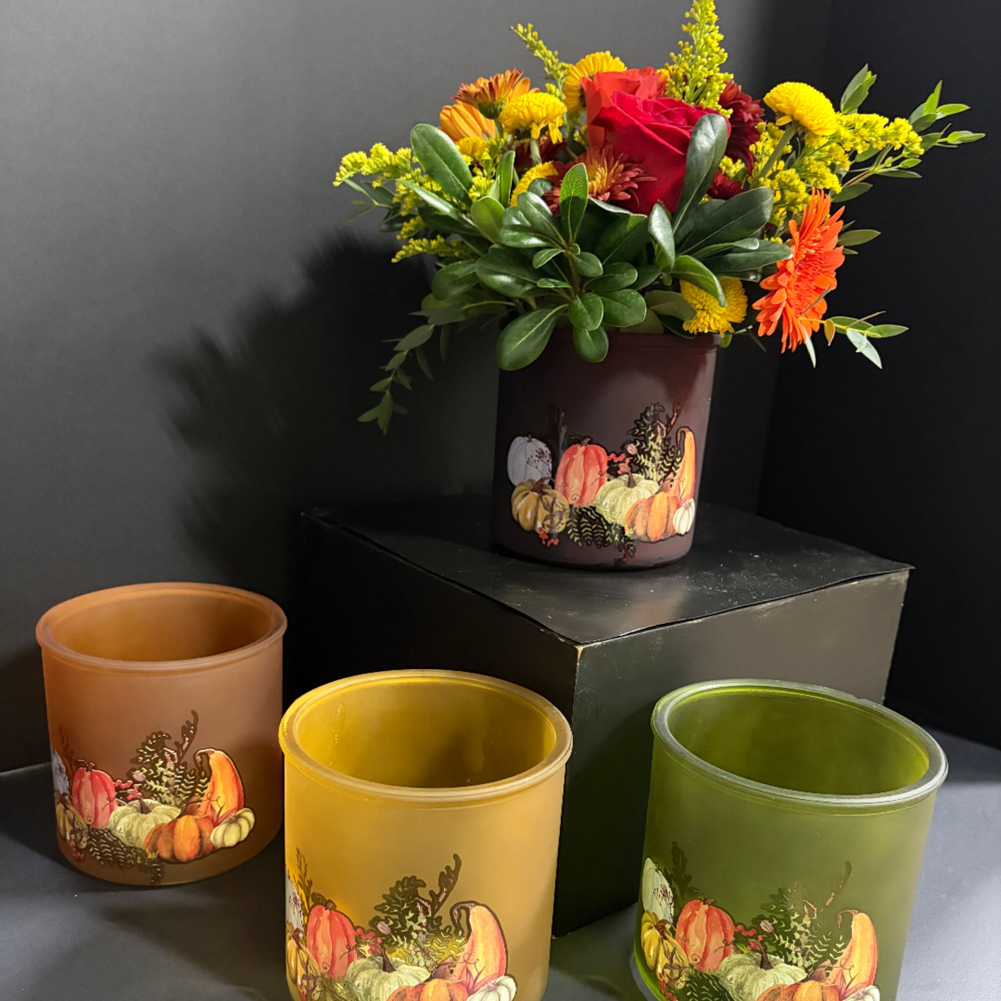 Fall floral arrangement in a pumpkin-decorated vase with yellow, orange, and red blooms
