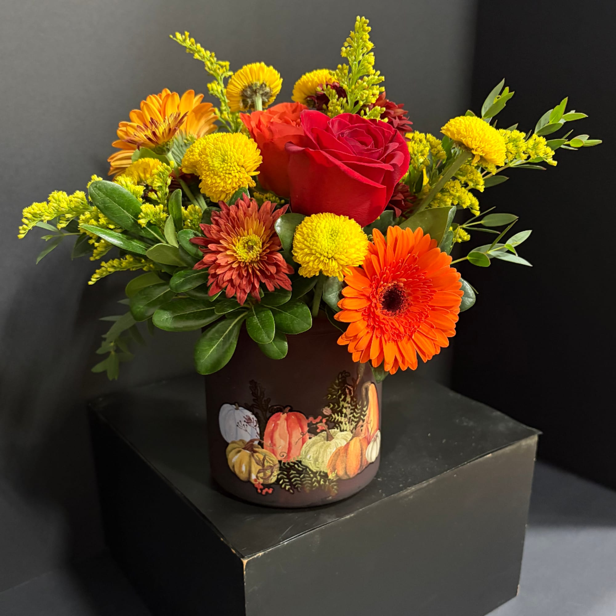 Mixed bouquet with a red rose and bright orange and yellow flowers in a pumpkin vase