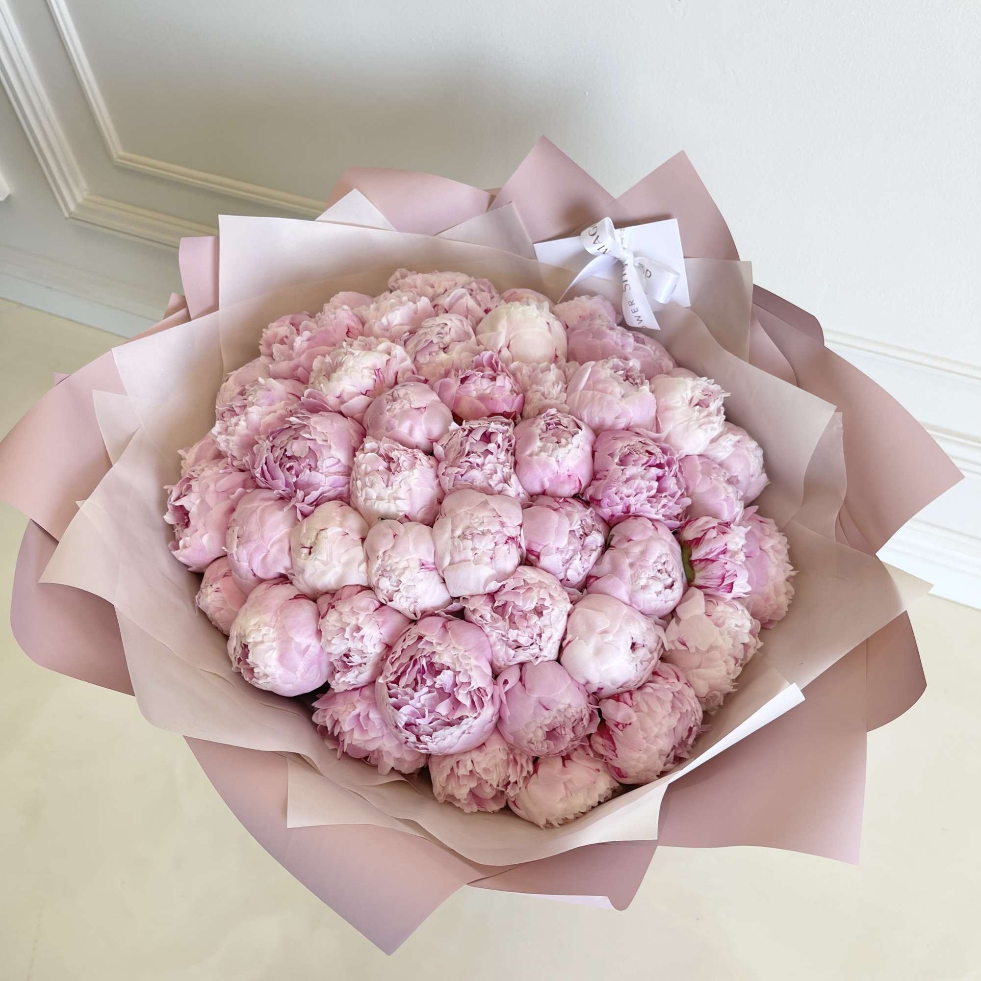 Large bouquet of pale pink peonies wrapped in pink paper