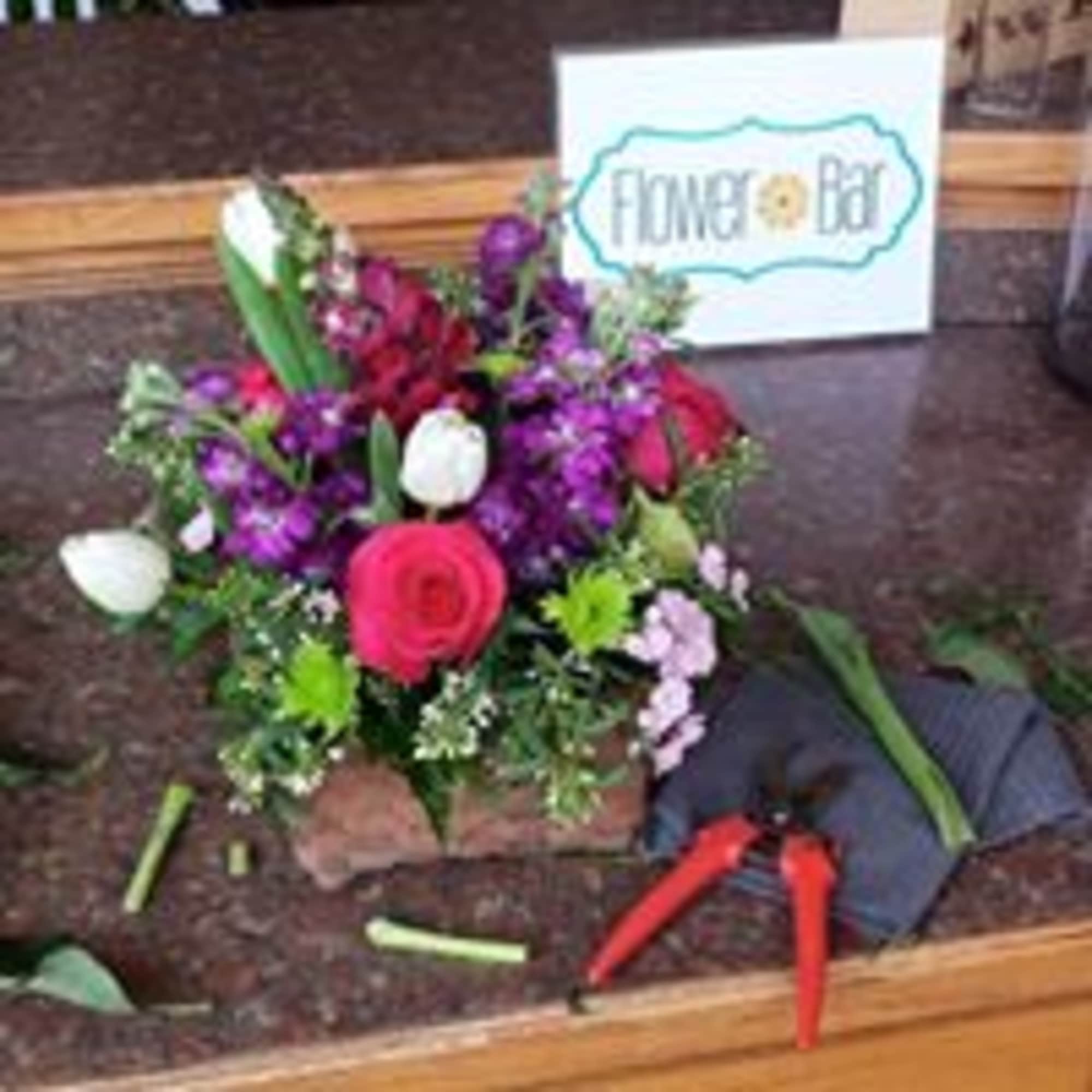 Mixed bouquet with roses and purple flowers beside a Flower Bar sign