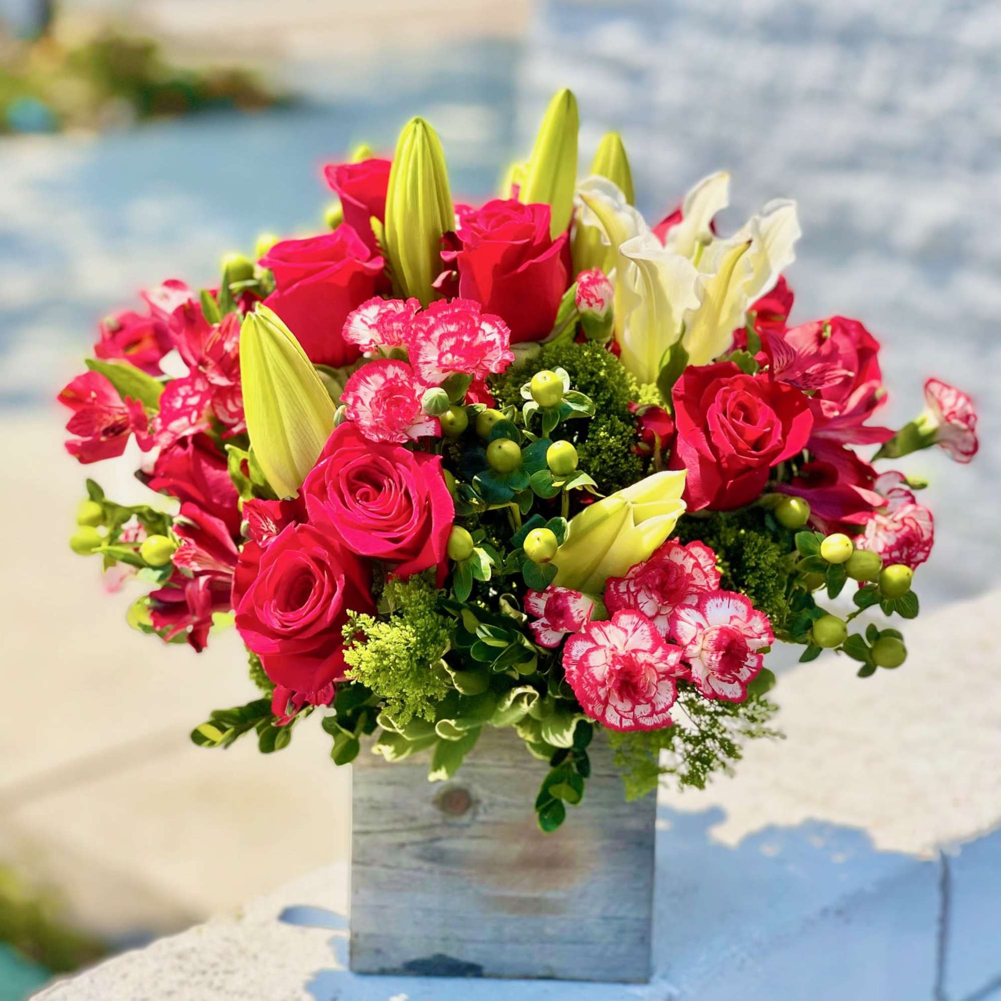Bright pink roses and lilies arranged in a square wooden vase