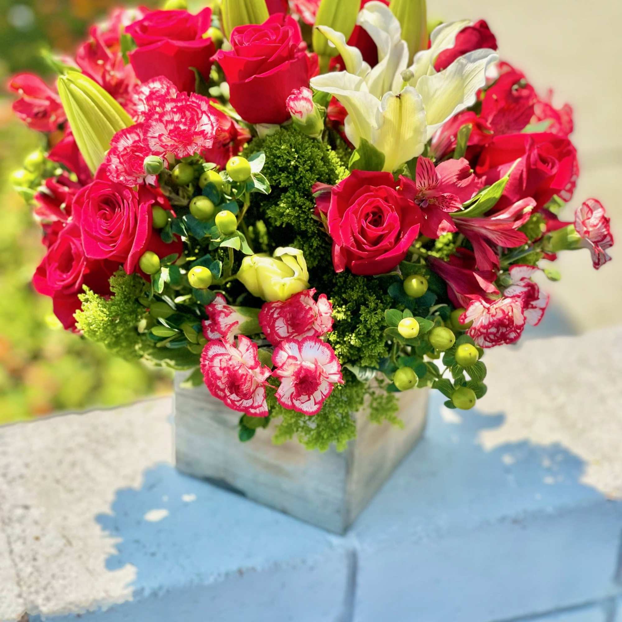 Bouquet of hot pink roses, white lilies, and carnations in a square vase