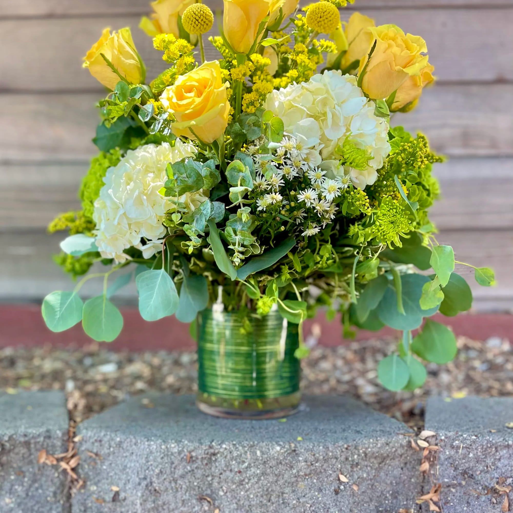 Yellow roses and white hydrangeas in a green glass vase