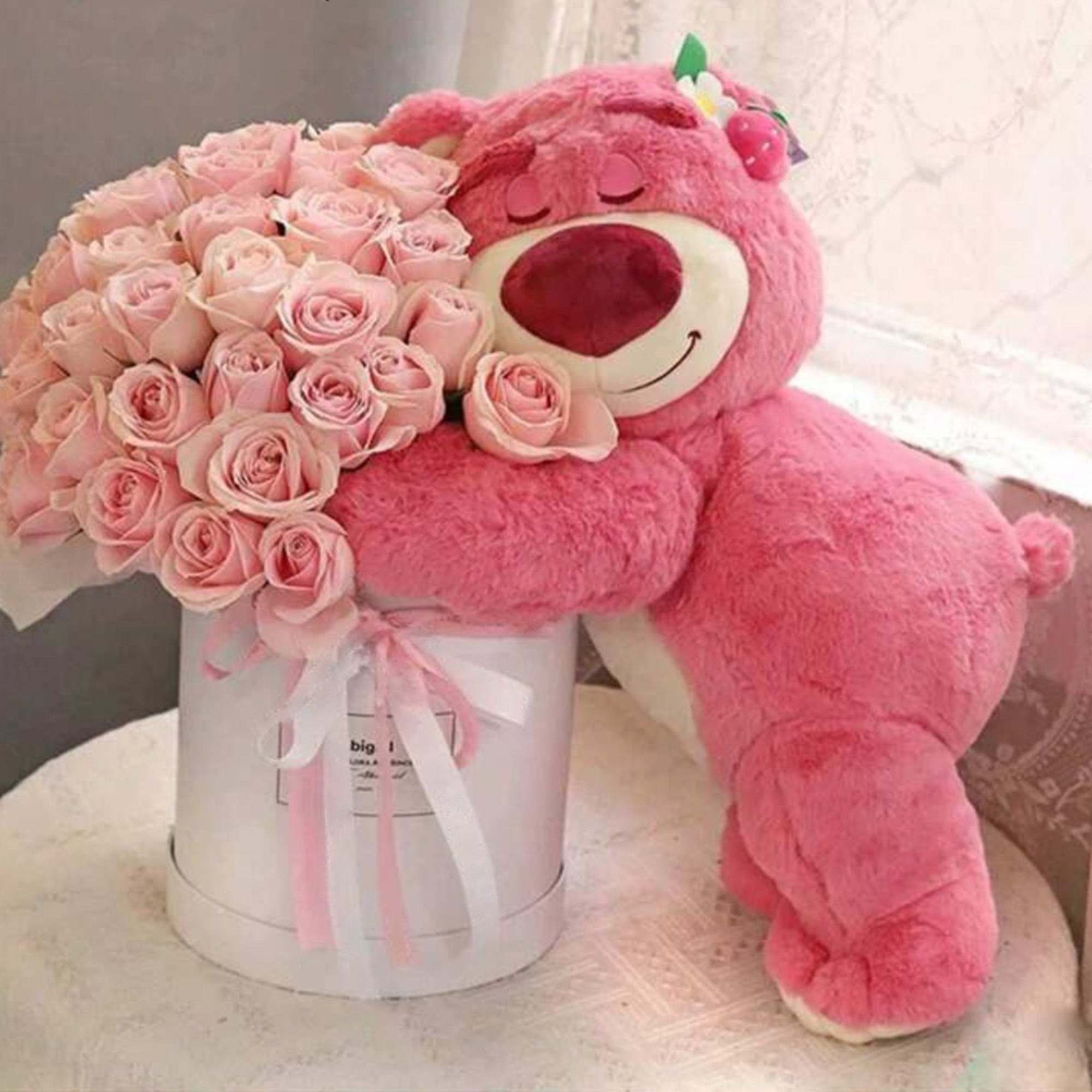 Pink teddy bear holding a bouquet of pale pink roses in a white box