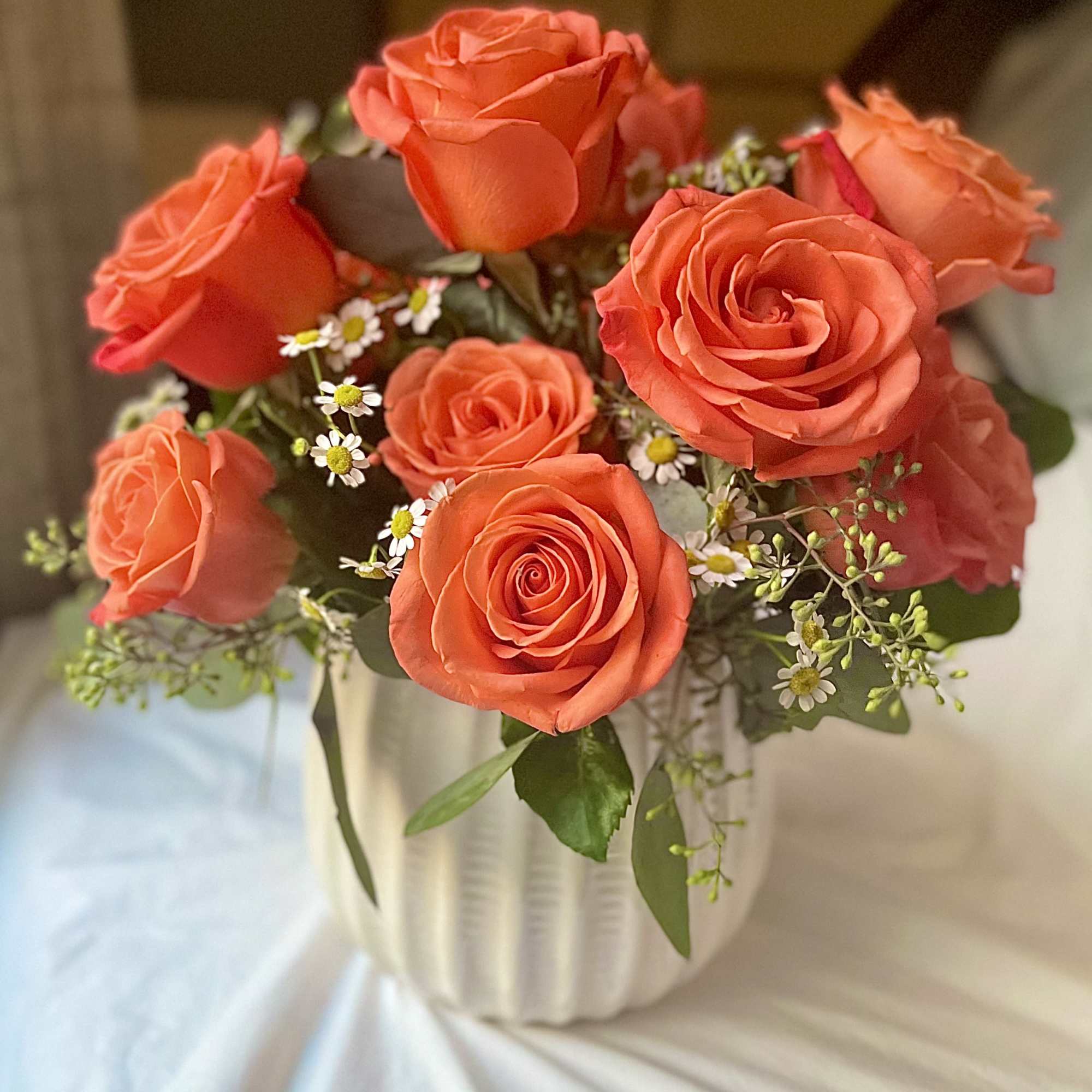 Orange roses arranged in a white vase with small white filler flowers