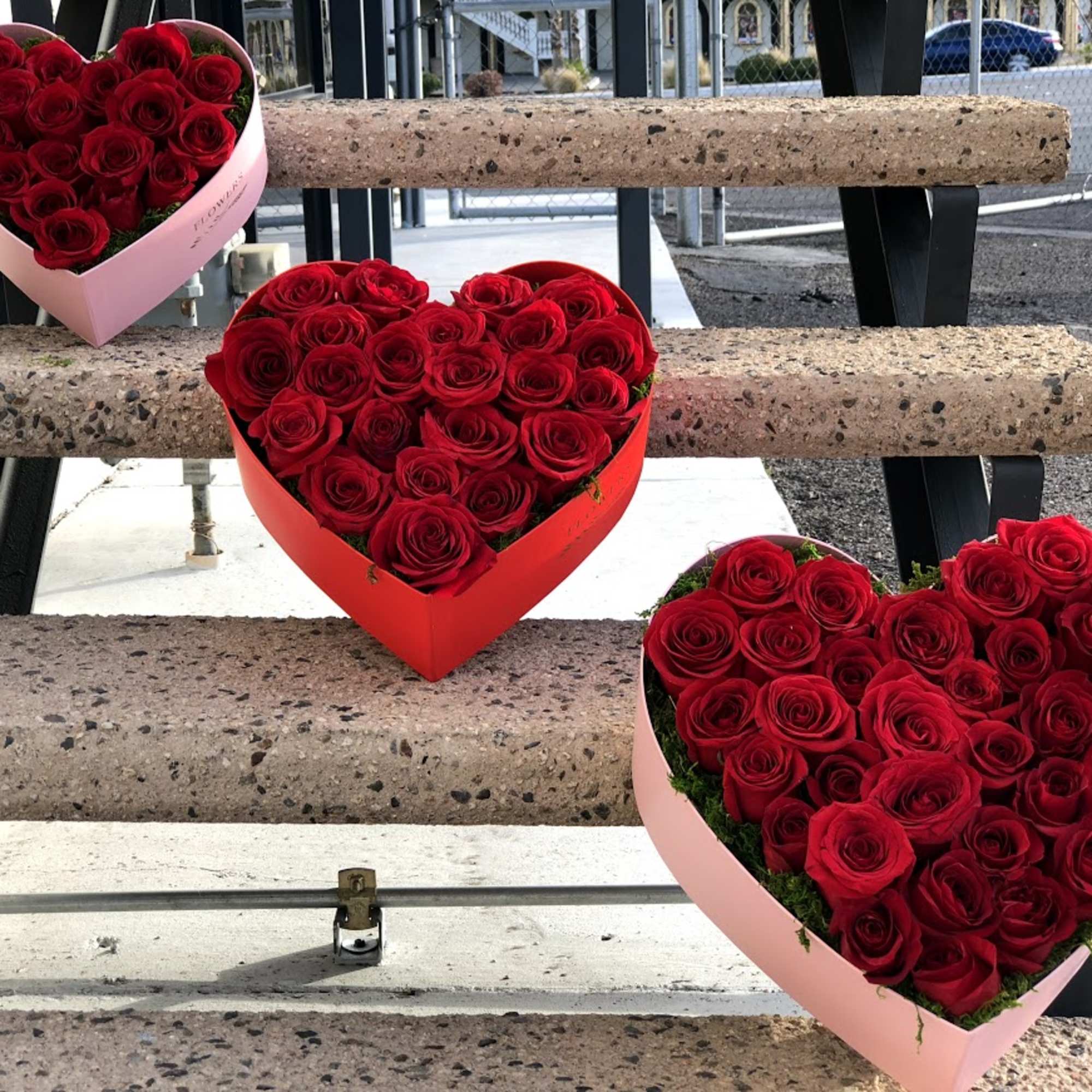Three heart-shaped boxes filled with red roses on outdoor steps