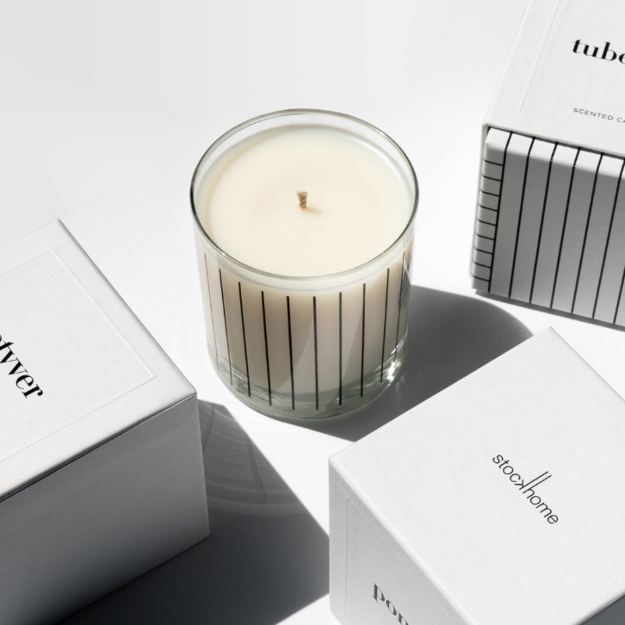 White scented candle in a clear glass jar with striped boxes around it