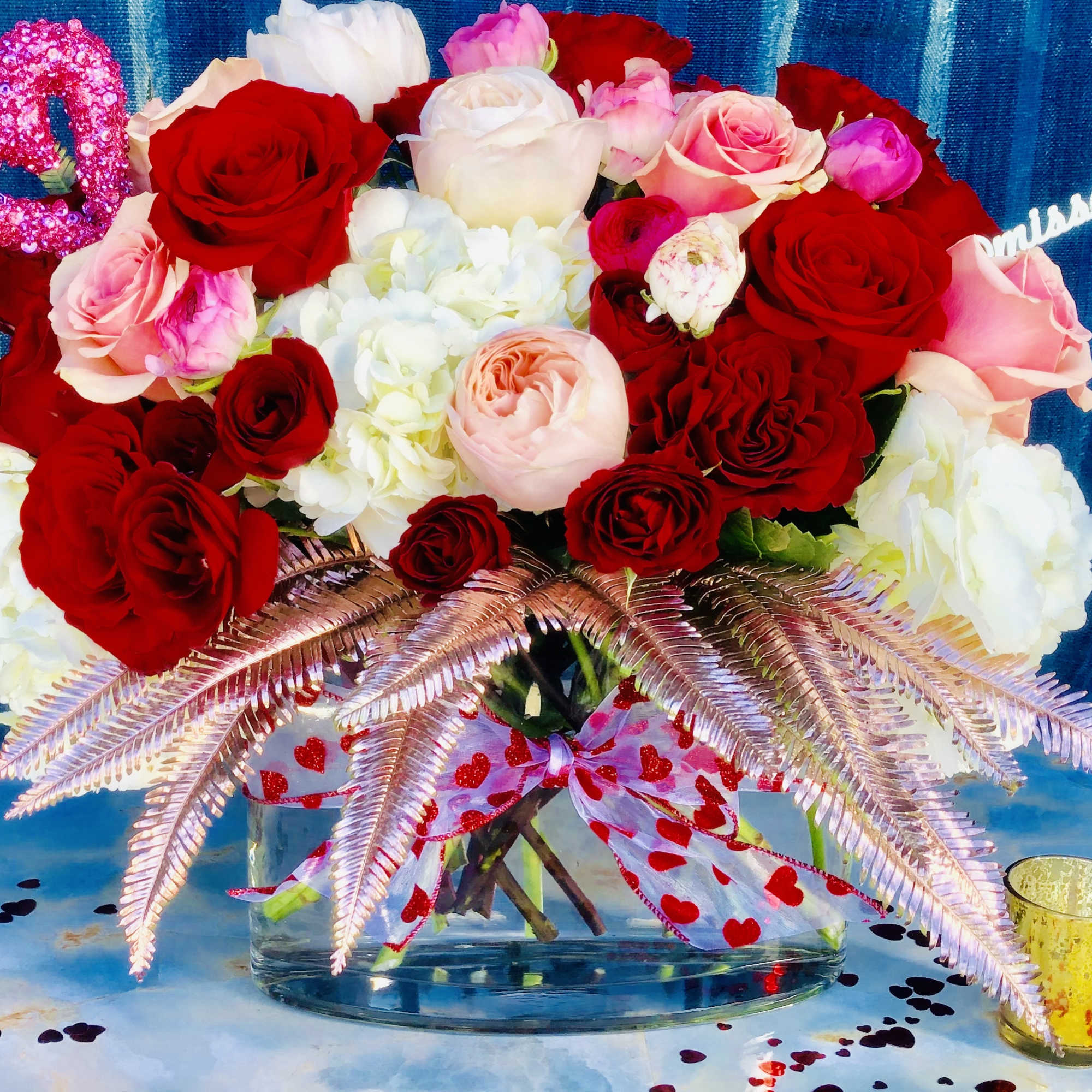 Bouquet of red, pink, and white roses in a glass vase with heart decorations