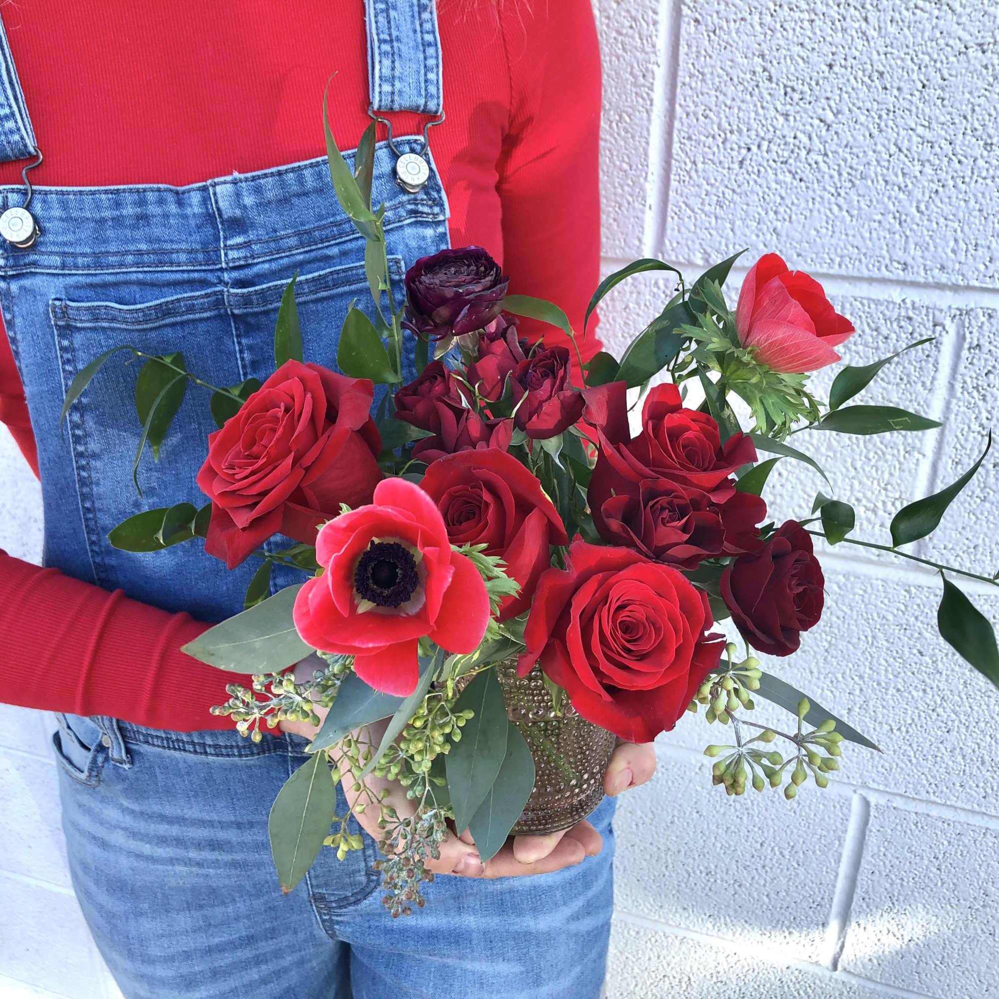 Handheld bouquet of red roses and a red anemone in a small vase