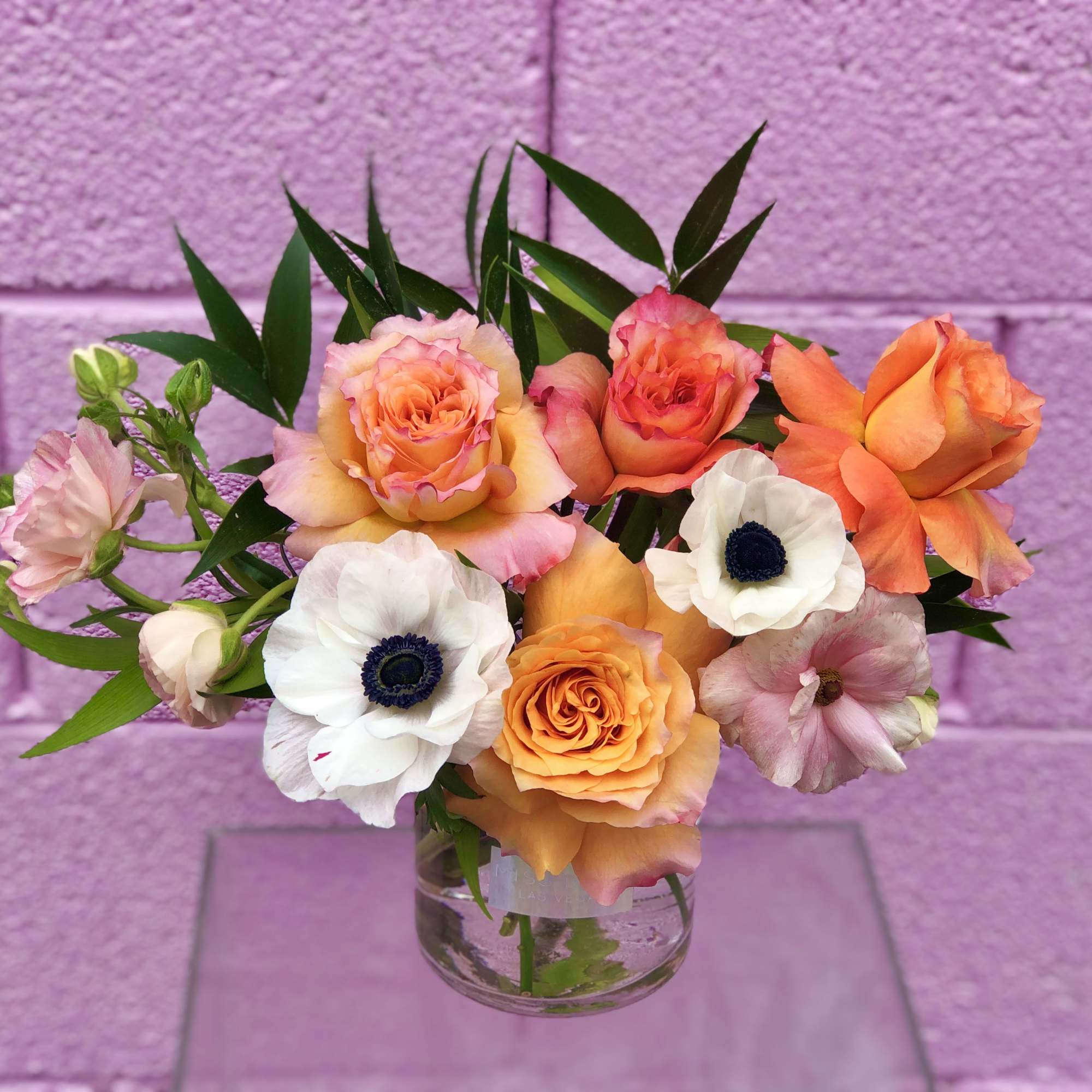Bouquet of orange and peach roses with white anemones in a clear glass vase
