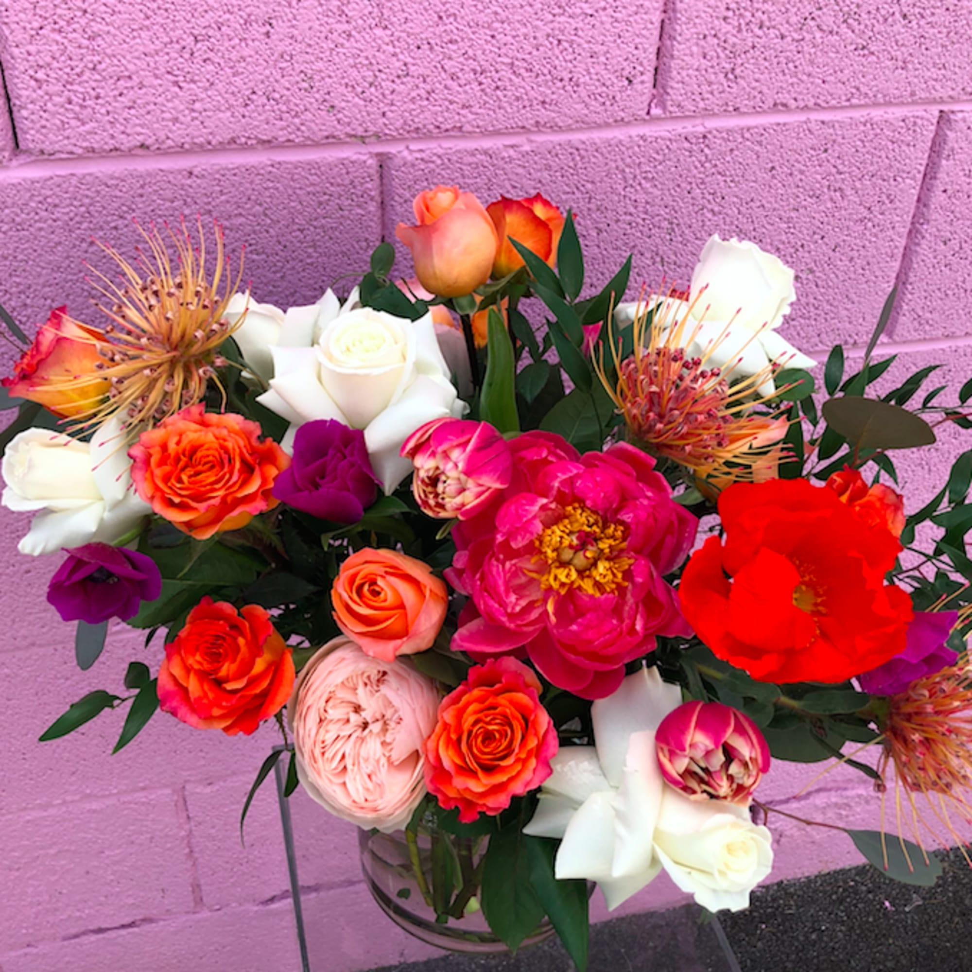 Mixed bouquet of roses, peonies, and protea in a glass vase