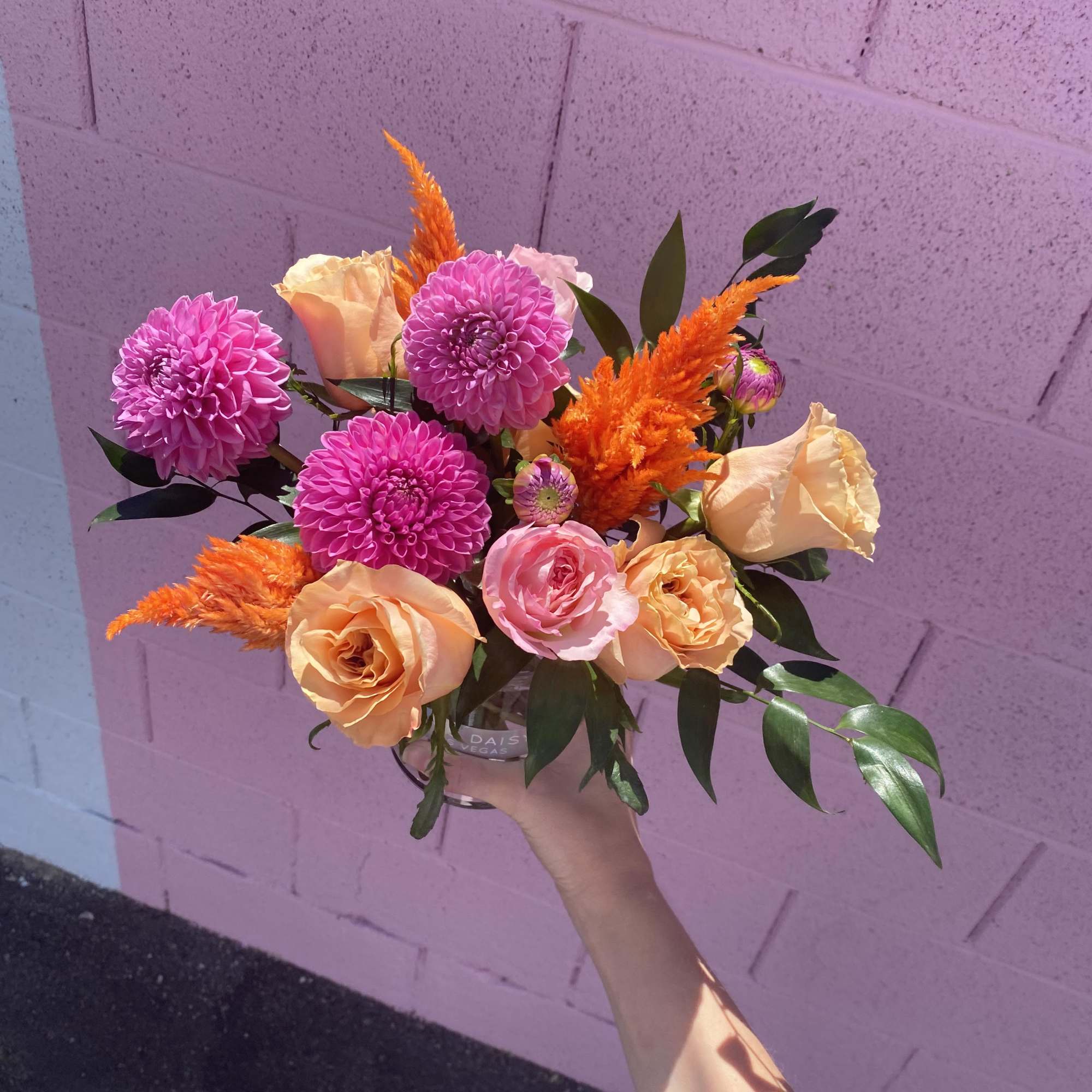 Handheld bouquet of pink and peach flowers with orange accents