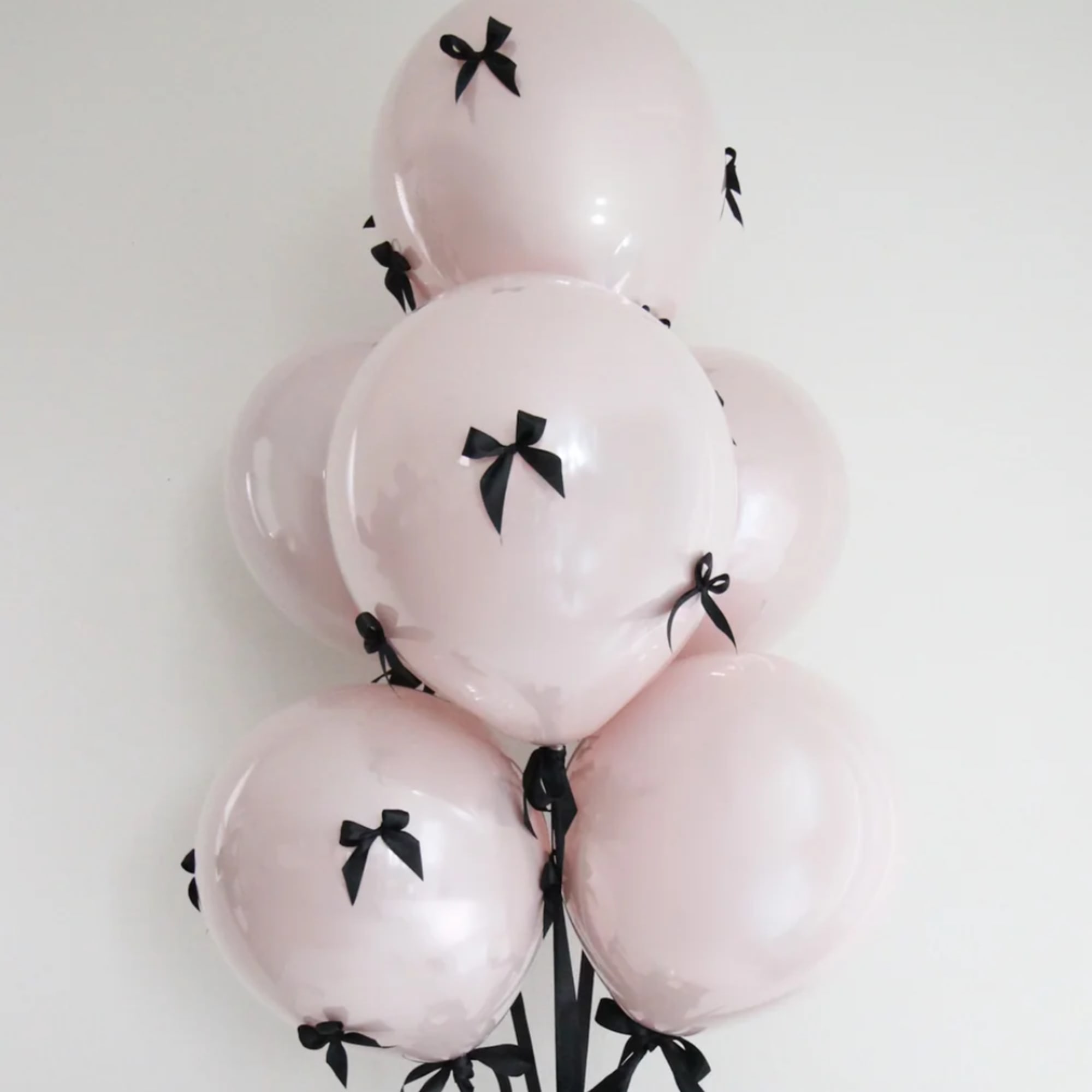 Cluster of pale pink balloons with black bows against a white wall