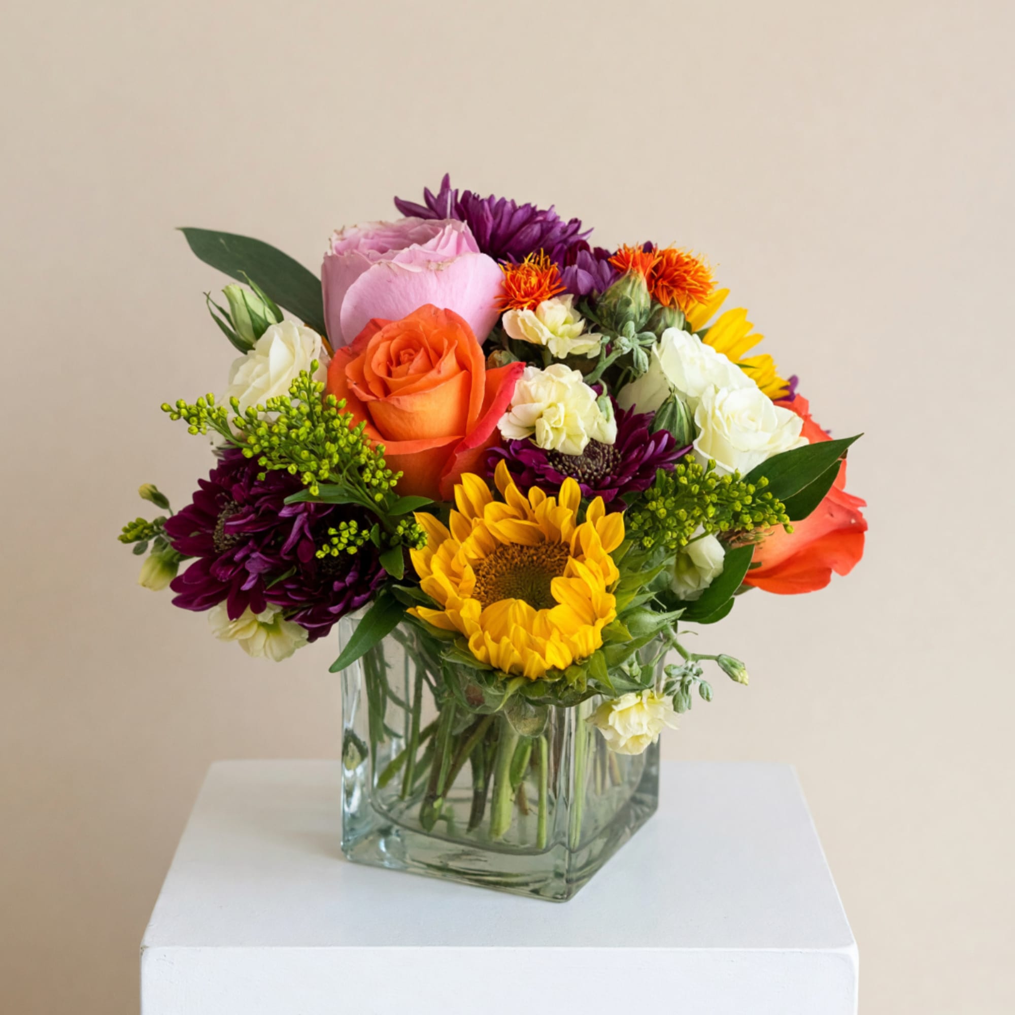 Mixed bouquet of roses, sunflowers, and chrysanthemums in a glass vase