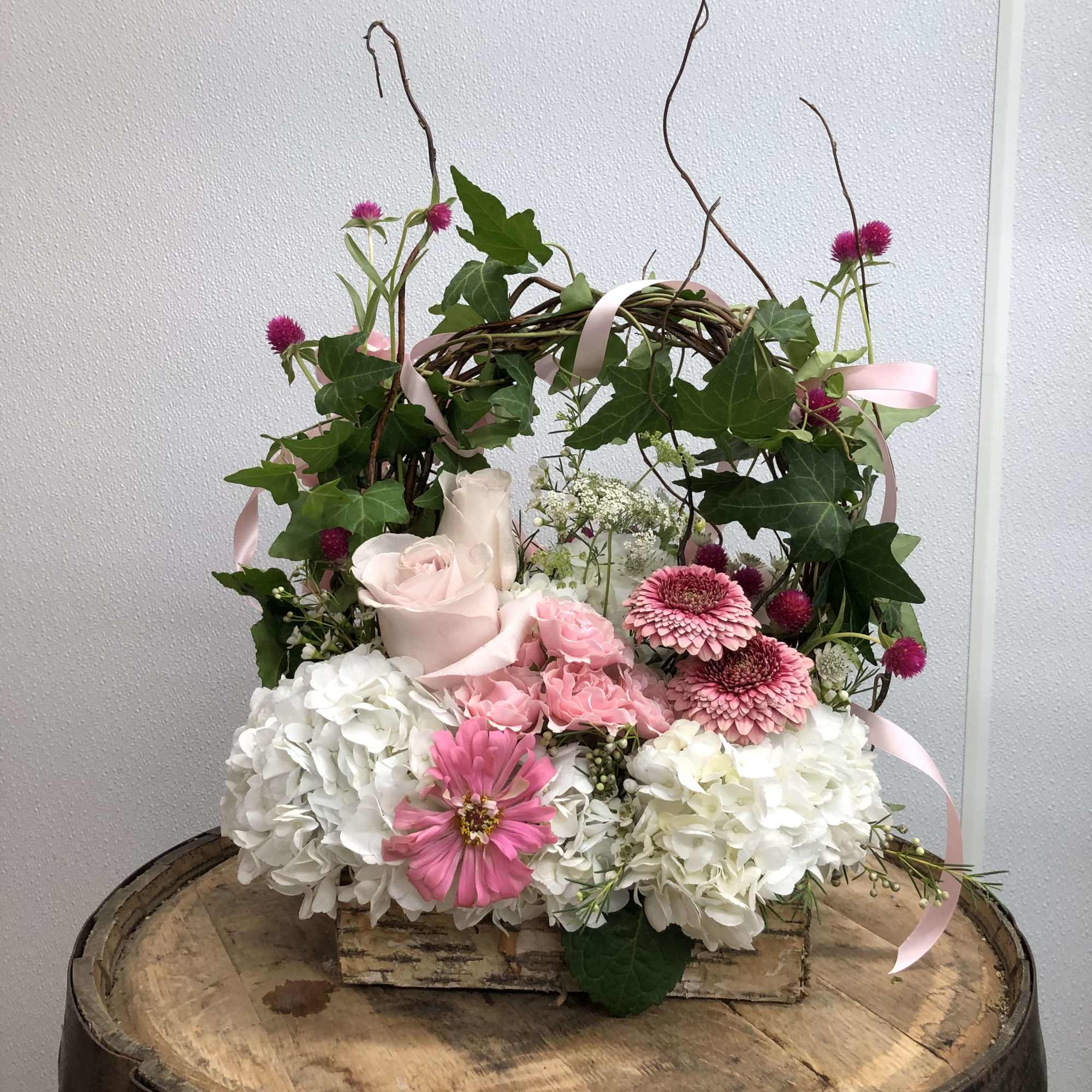 Pink and white floral arrangement in a woven basket with ribbon