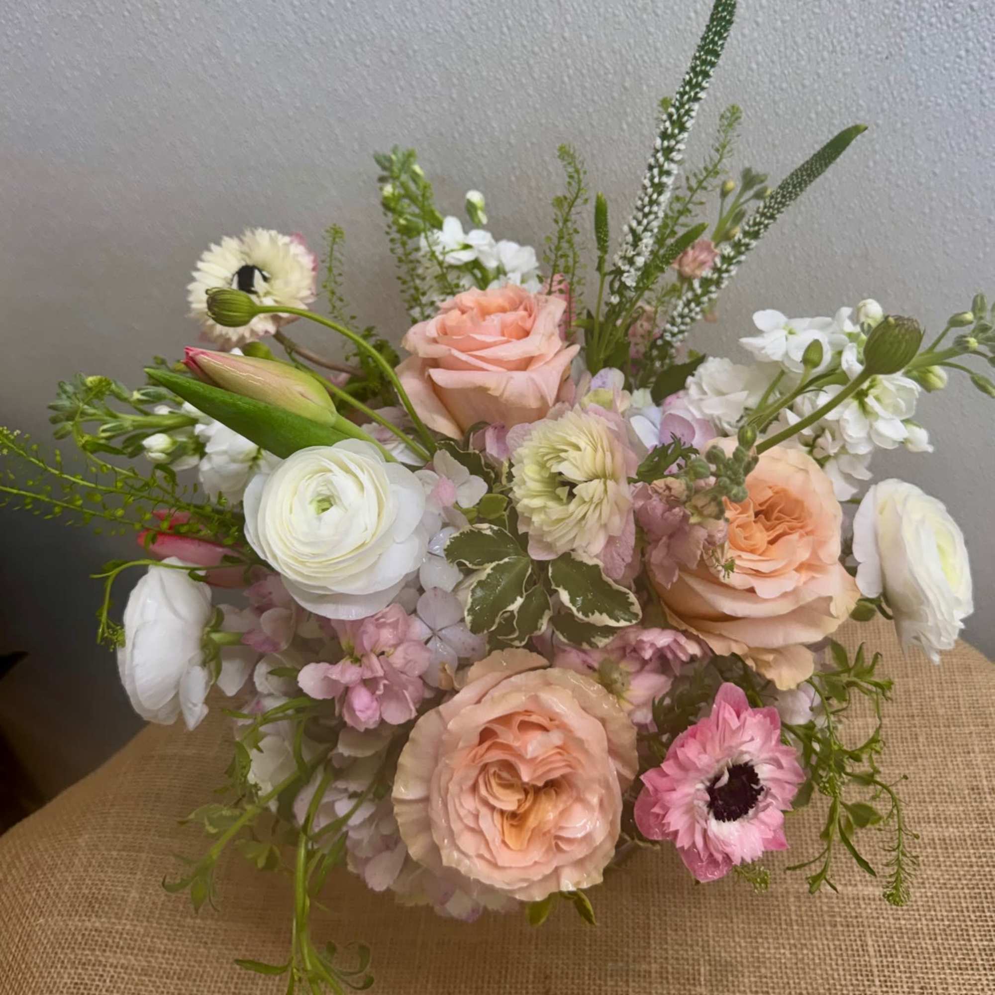 A soft, pastel arrangement built around peach roses and white ranunculus creates, photo 2 of 2