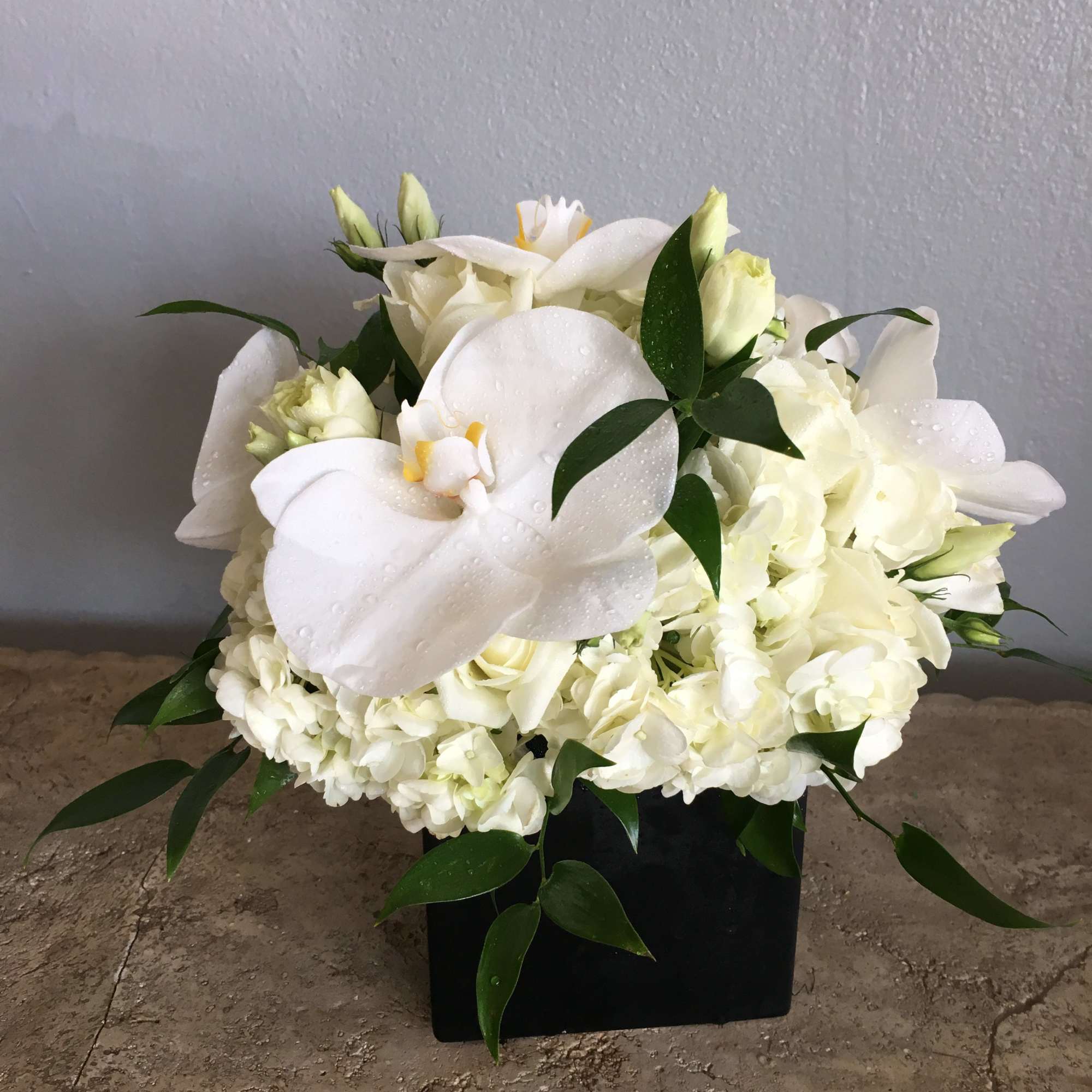 White floral arrangement with calla lilies and hydrangeas in a black container