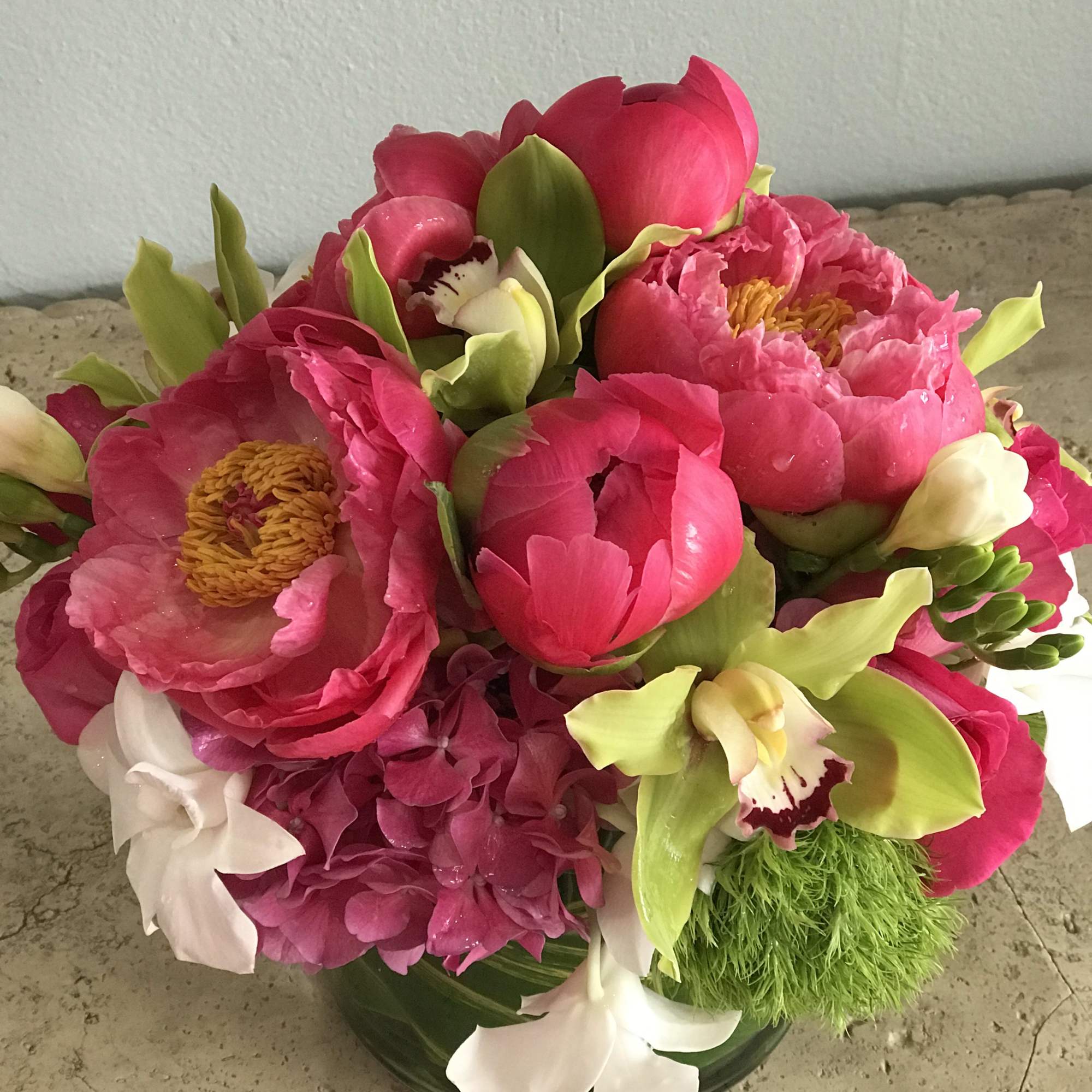 Pink peonies and green orchids in a low glass bowl
