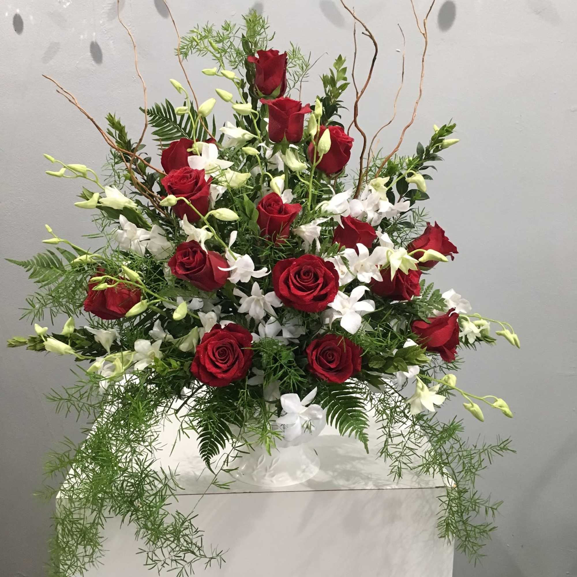 Red roses and white orchids in a tall white vase with trailing greenery