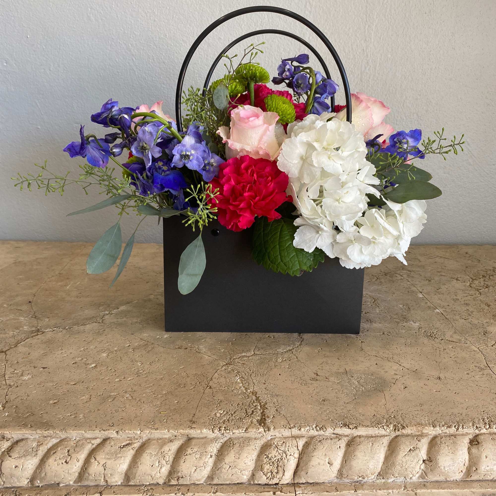 Mixed flower arrangement in a black handled box with blue, pink, white, and red blooms