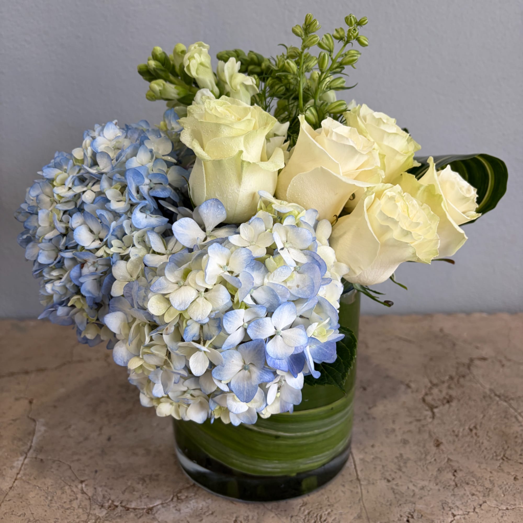 Blue hydrangeas and cream roses arranged in a green glass vase