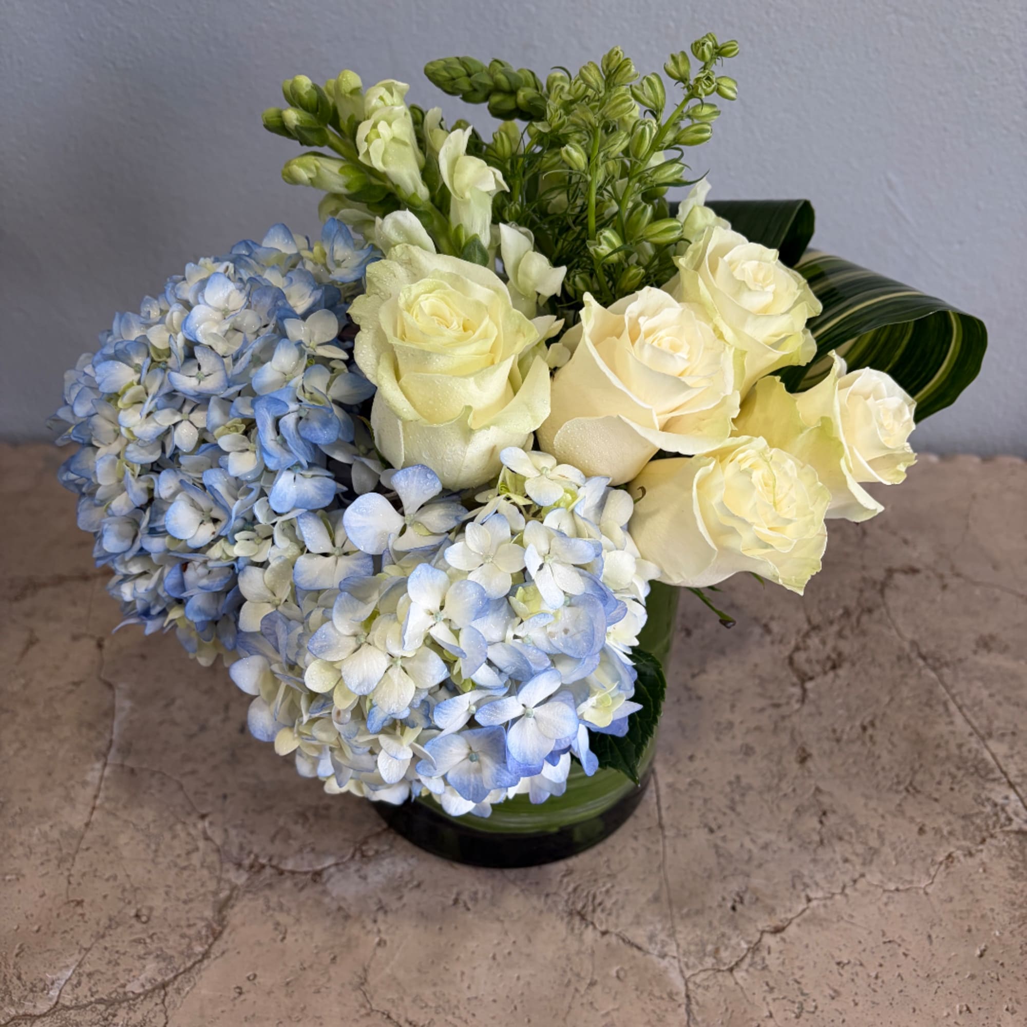Blue hydrangeas and cream roses arranged in a glass vase