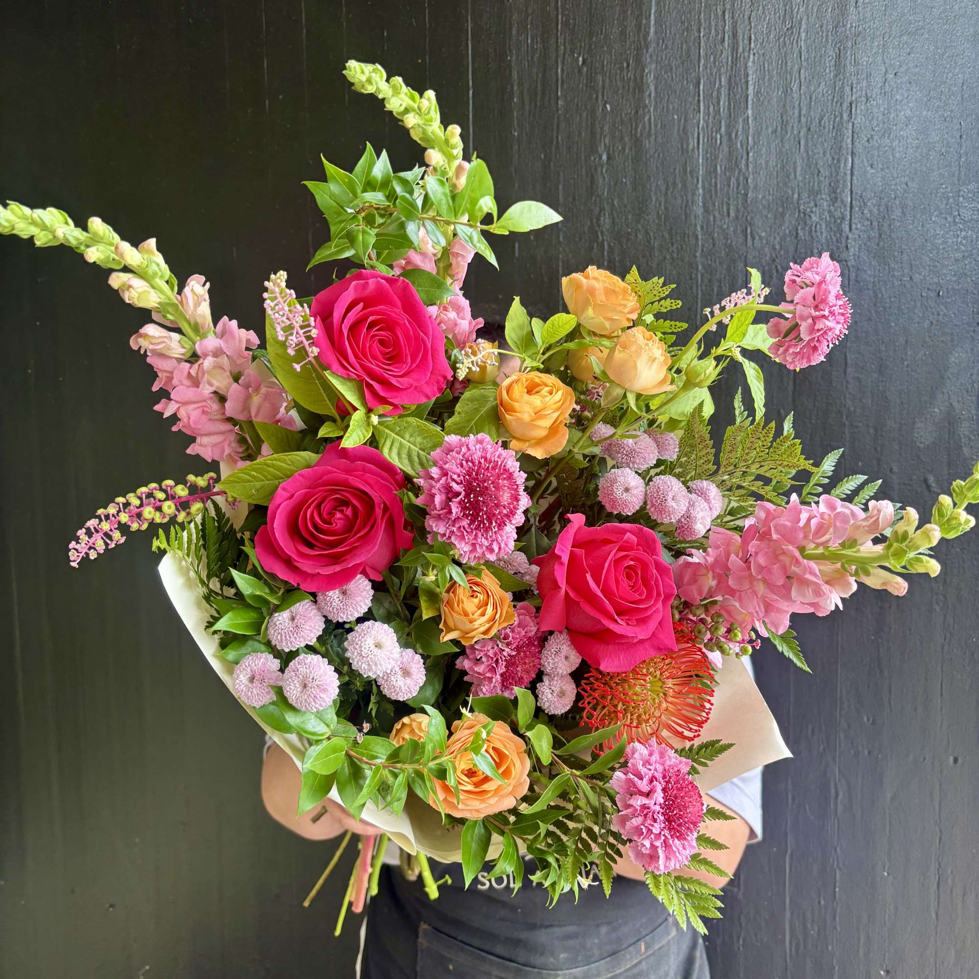 Handheld bouquet of pink and orange roses with mixed blooms