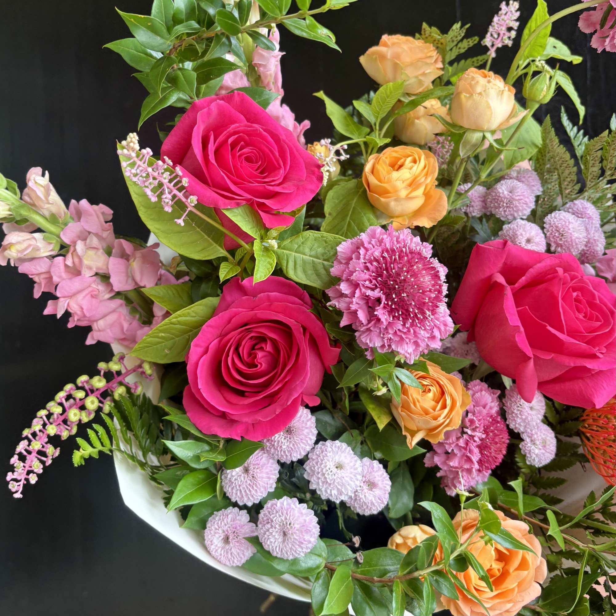 Bouquet of hot pink and peach roses with pink pompon flowers in a white vase