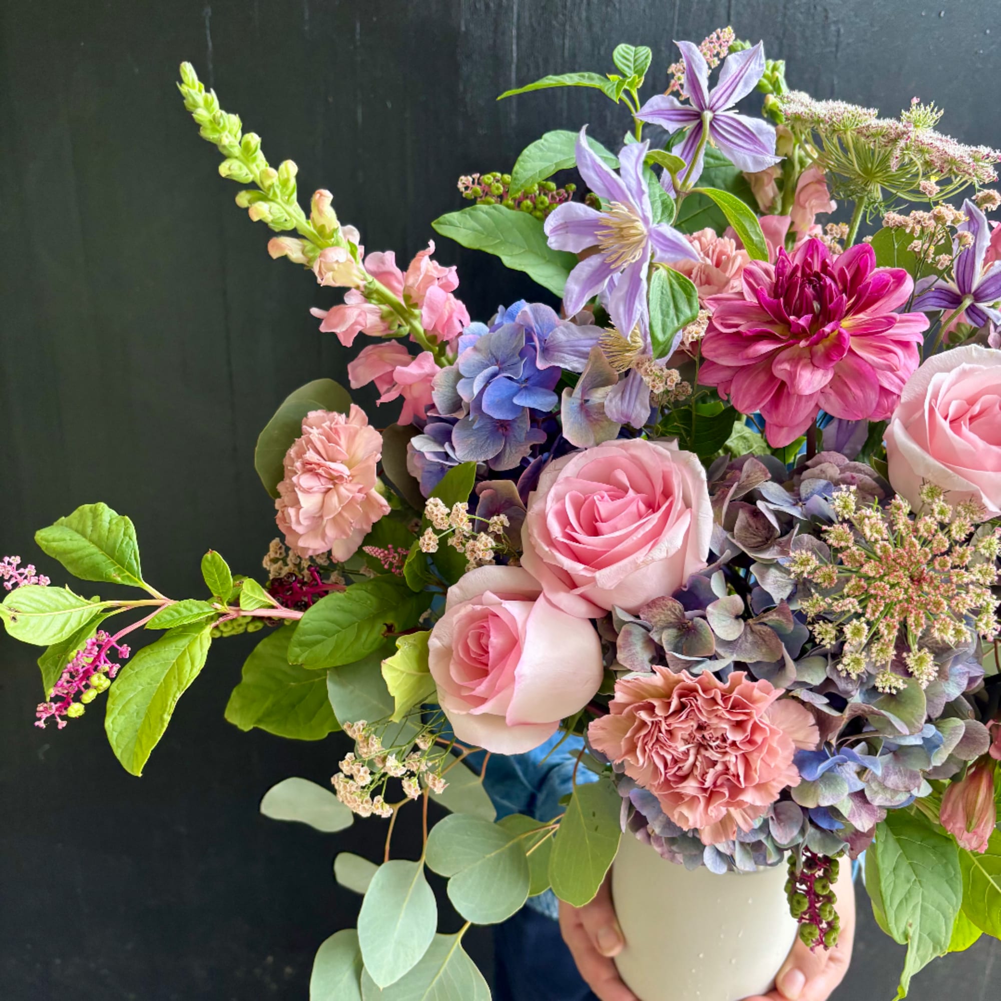 Mixed bouquet of pink roses, hydrangeas, and purple flowers in a white vase