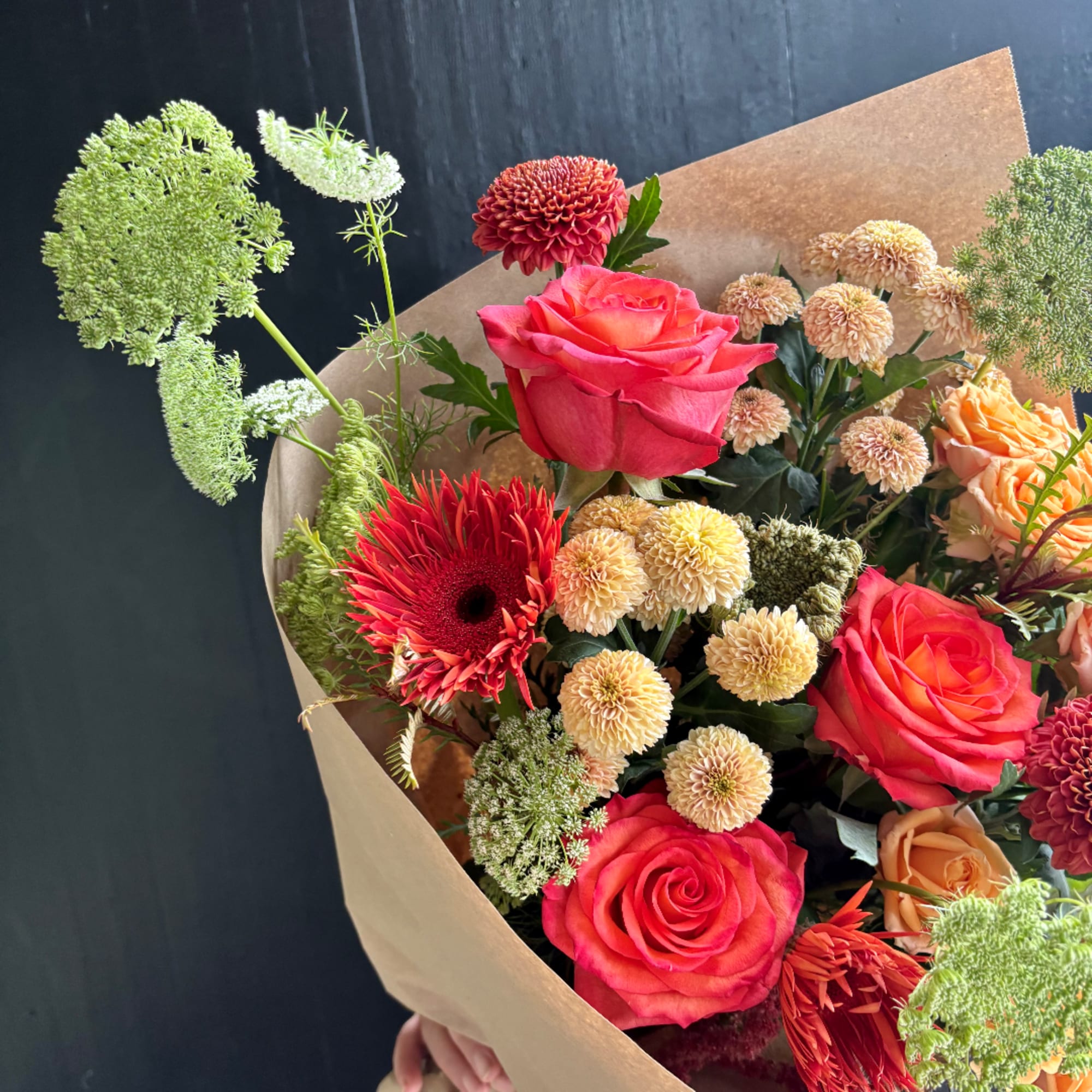 Bouquet of pink and orange roses with mixed chrysanthemums in brown paper