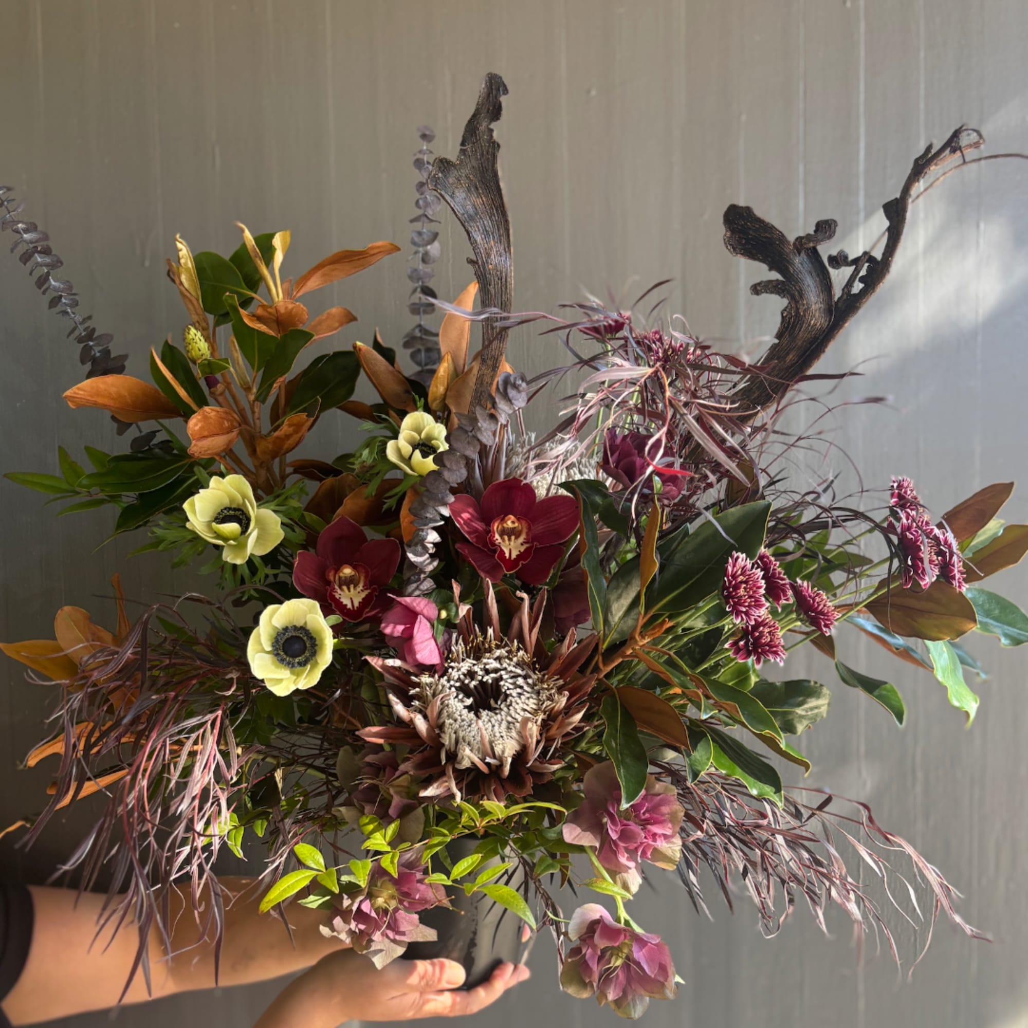 Handheld bouquet with burgundy and pale yellow flowers in a dramatic, sculptural design
