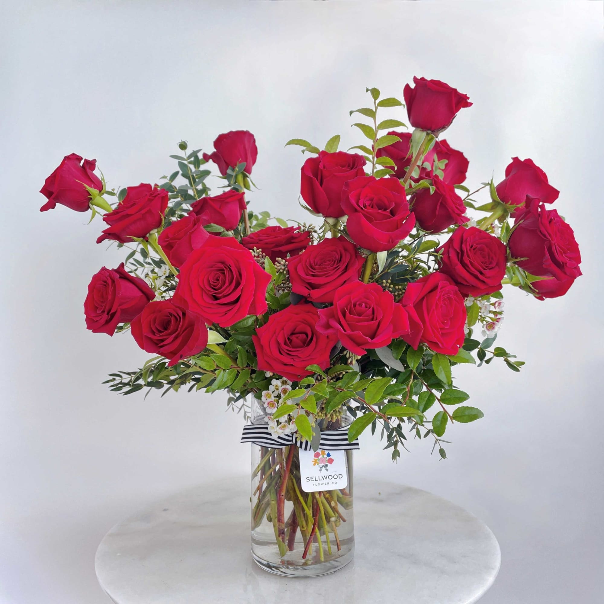 Red roses arranged in a clear glass vase with greenery