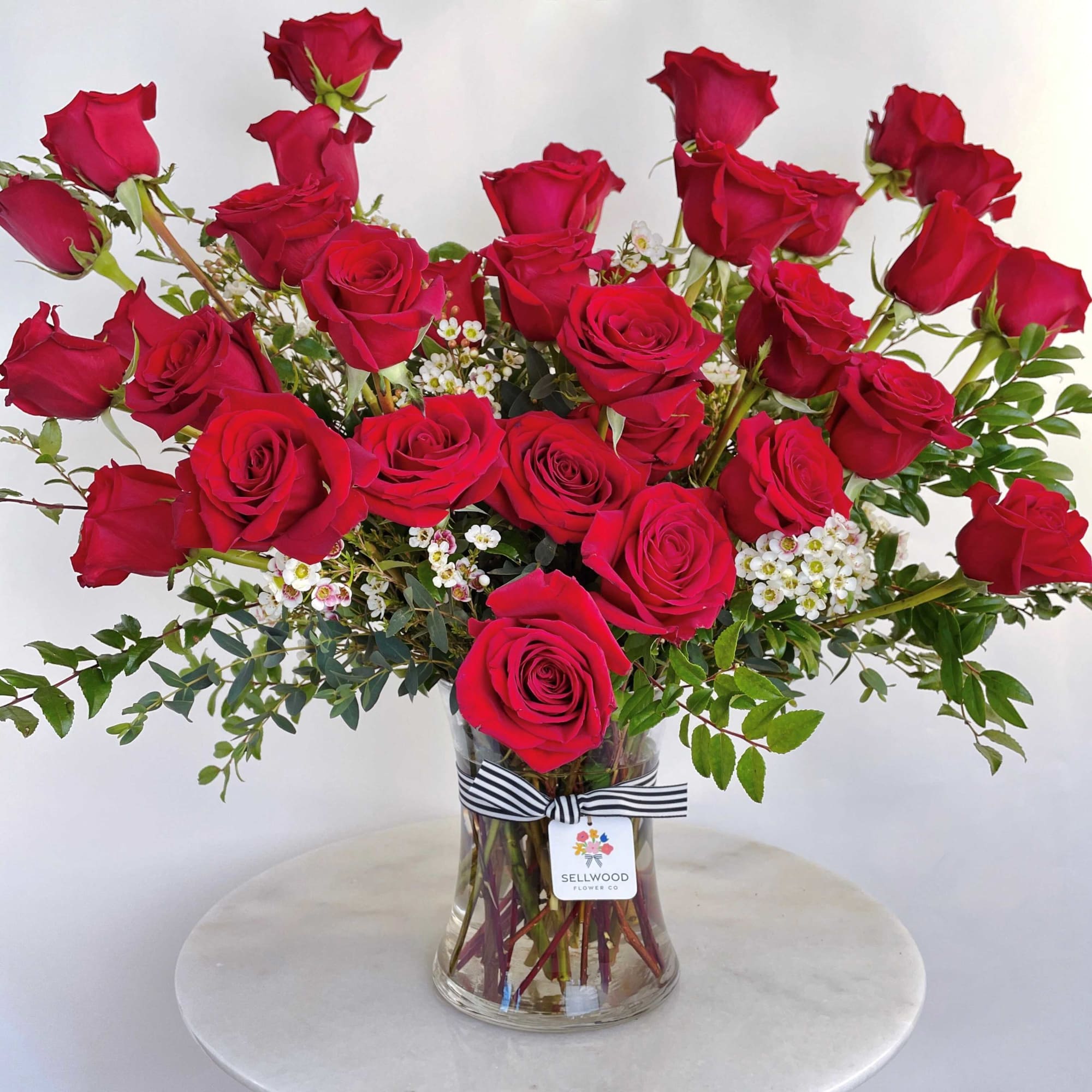 Red roses arranged in a clear glass vase with small white filler flowers