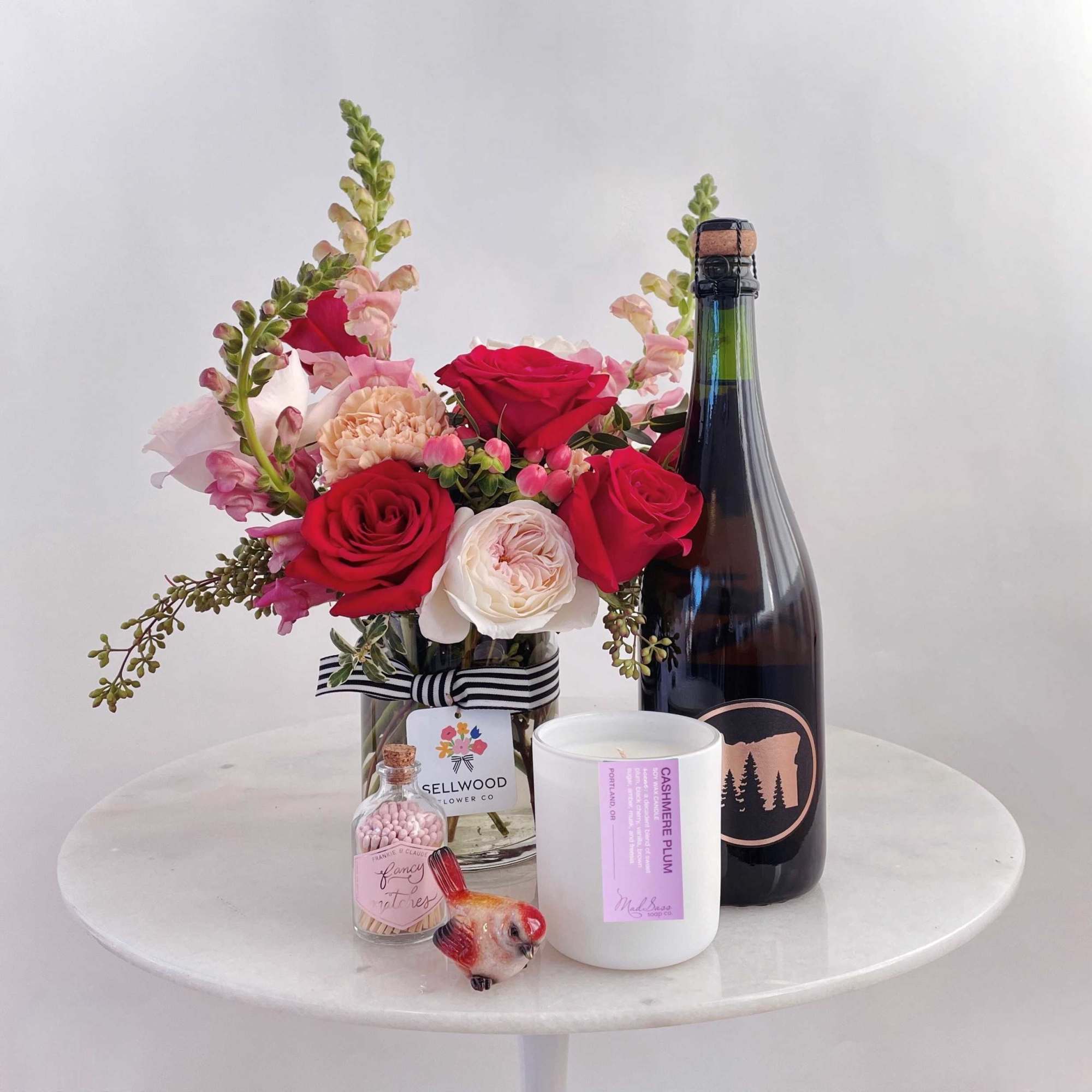Bouquet of red and blush roses in a glass vase with a champagne bottle and candle