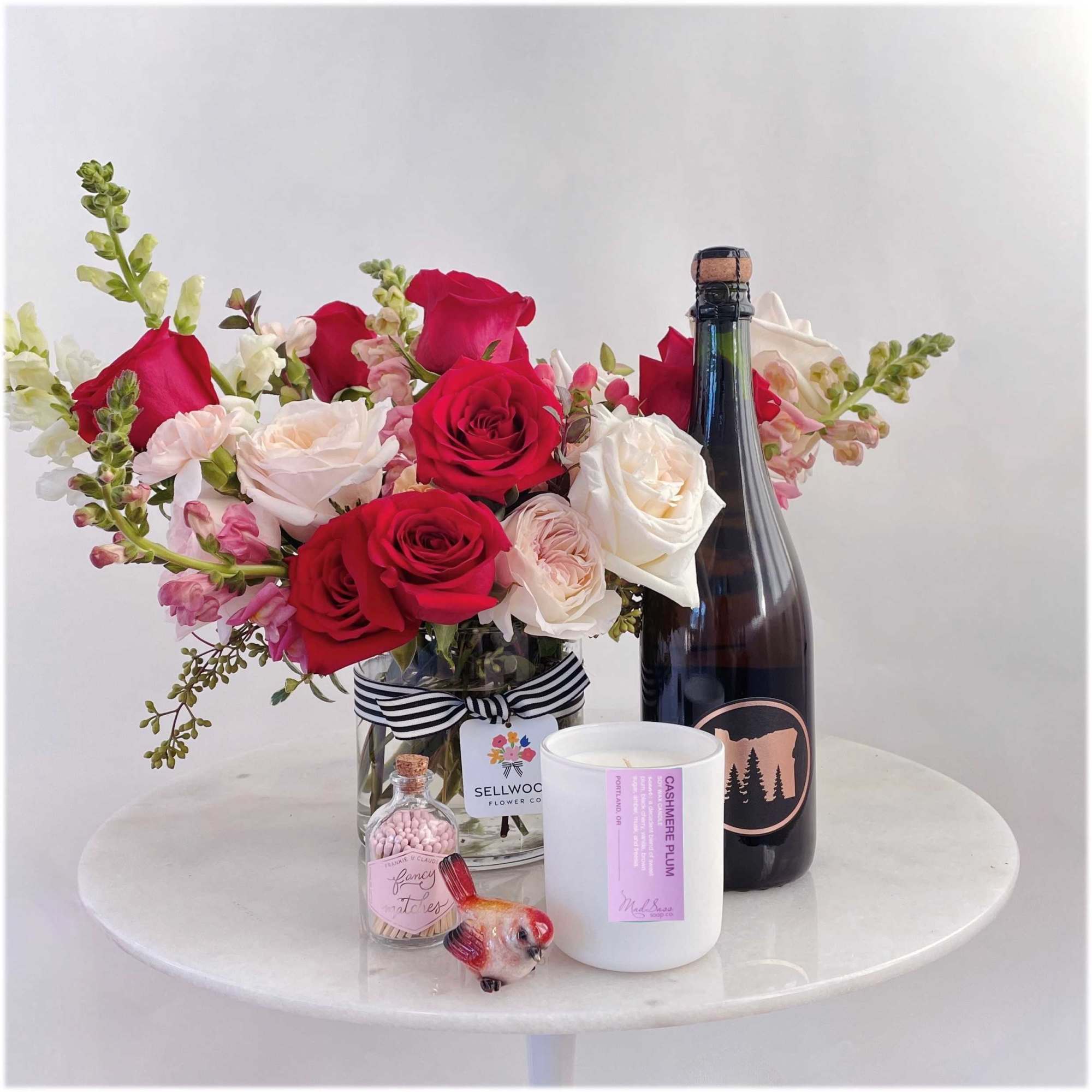 Bouquet of red and white roses in a glass vase with a champagne bottle and candle.