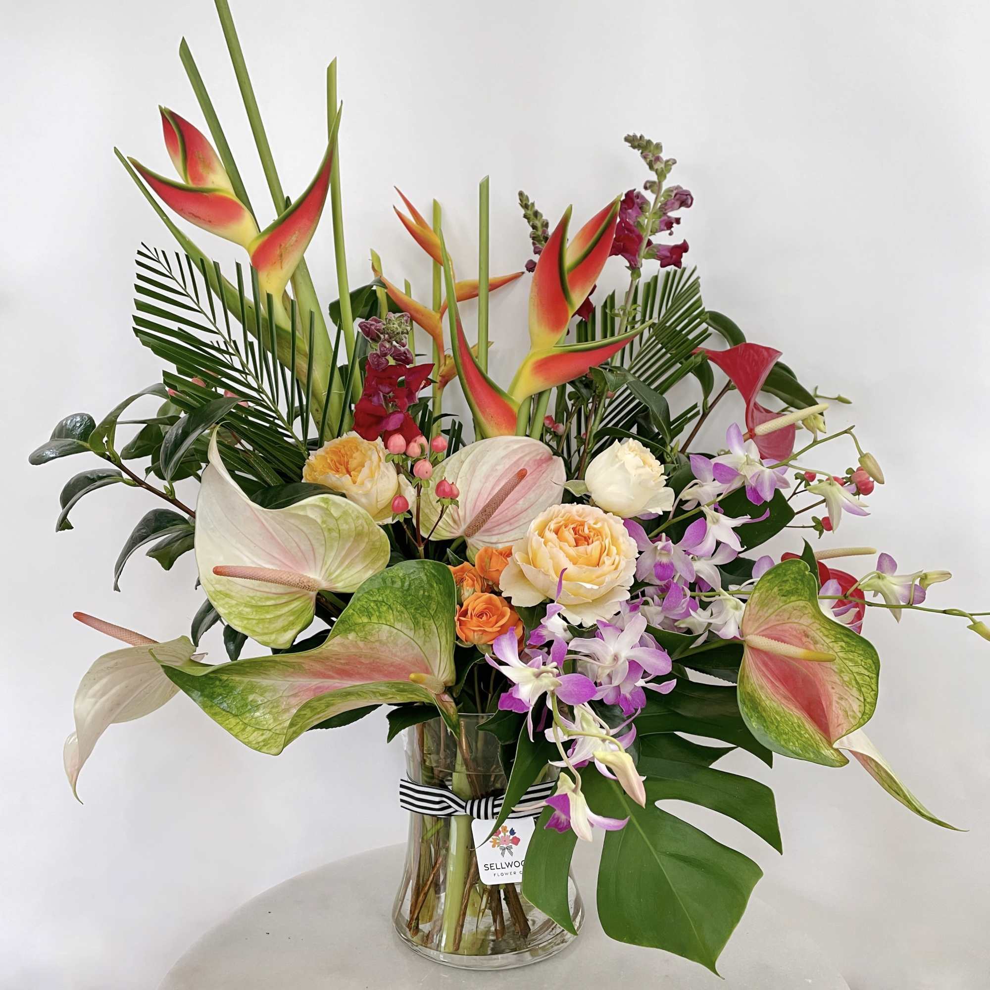 Tropical bouquet in a glass vase with pink orchids and red heliconia