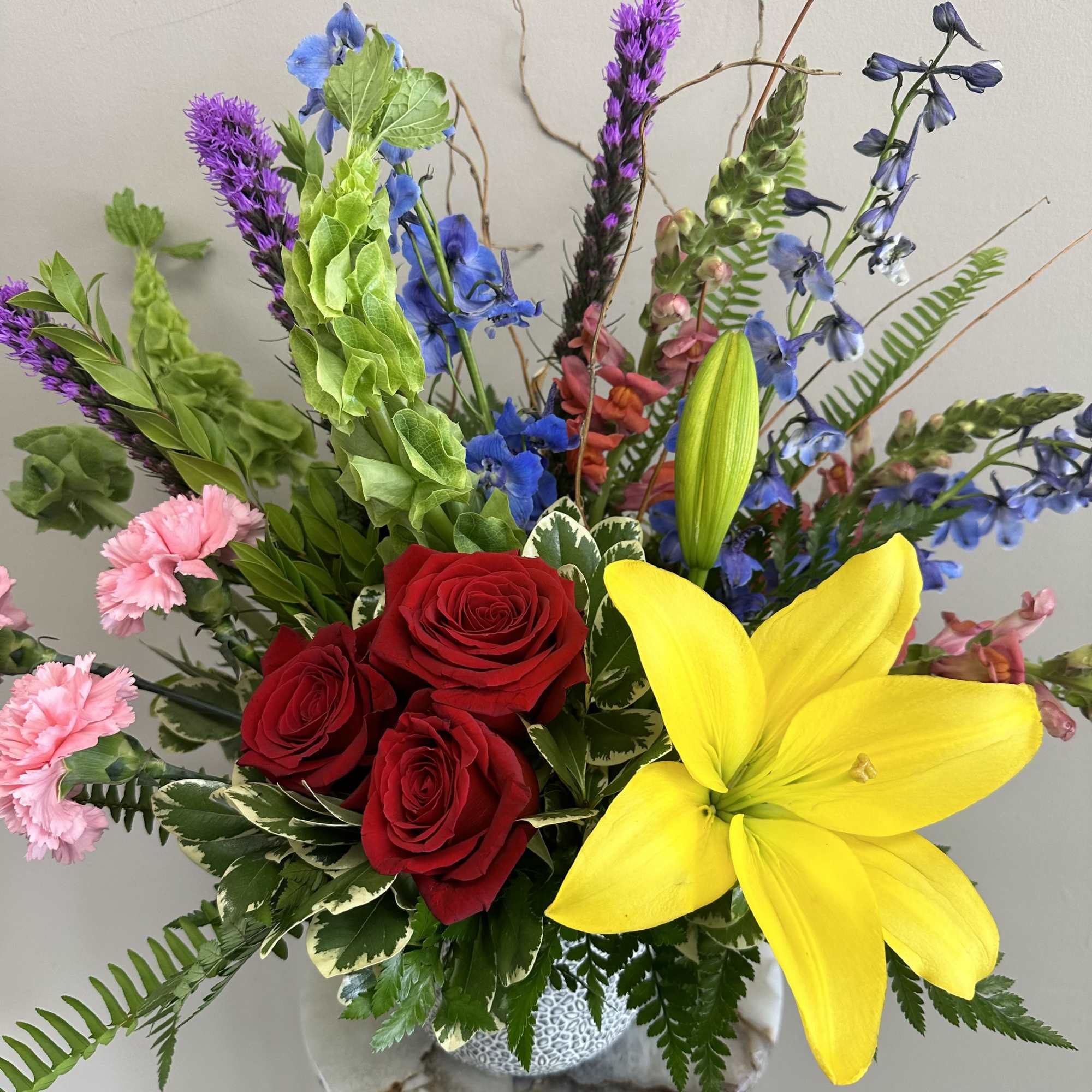 Mixed bouquet with red roses, a yellow lily, and blue and pink flowers in a vase
