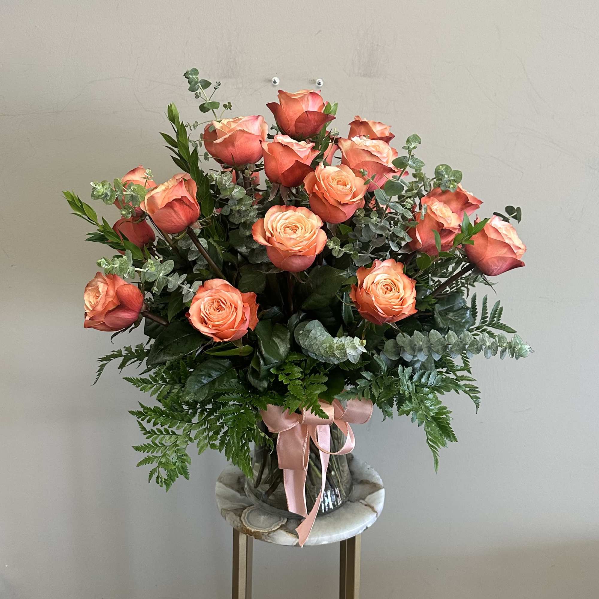 Bouquet of coral roses in a glass vase with a pink ribbon