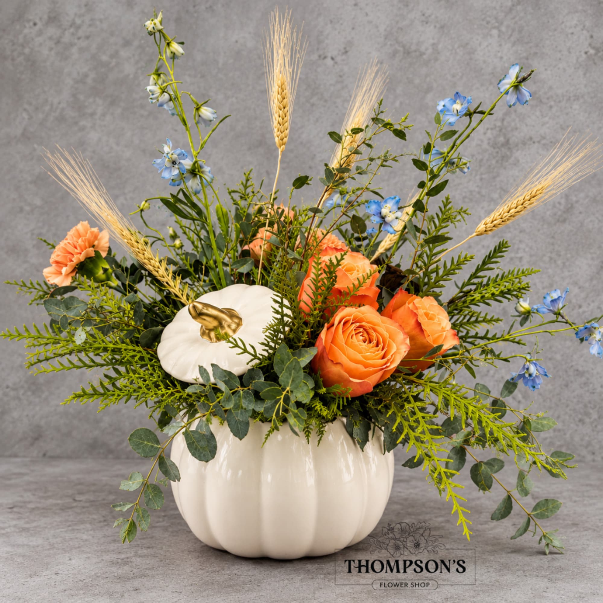 Orange roses and blue flowers in a white pumpkin vase