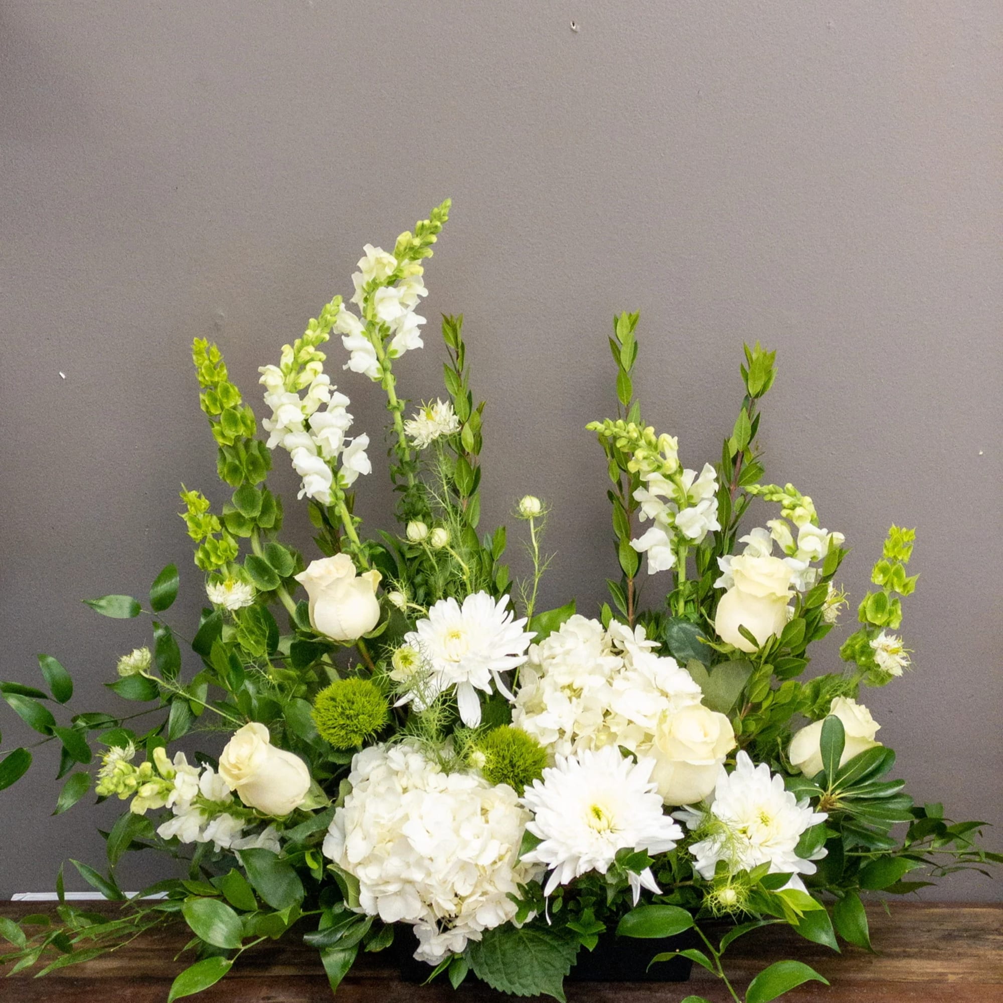 Low white and green floral arrangement with roses, hydrangeas, snapdragons, and mums in a rectangular container