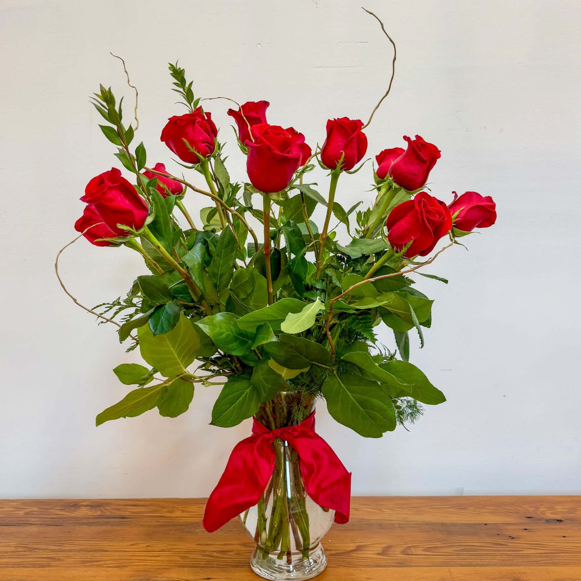 Tall arrangement of red roses in a clear glass vase with a red ribbon bow
