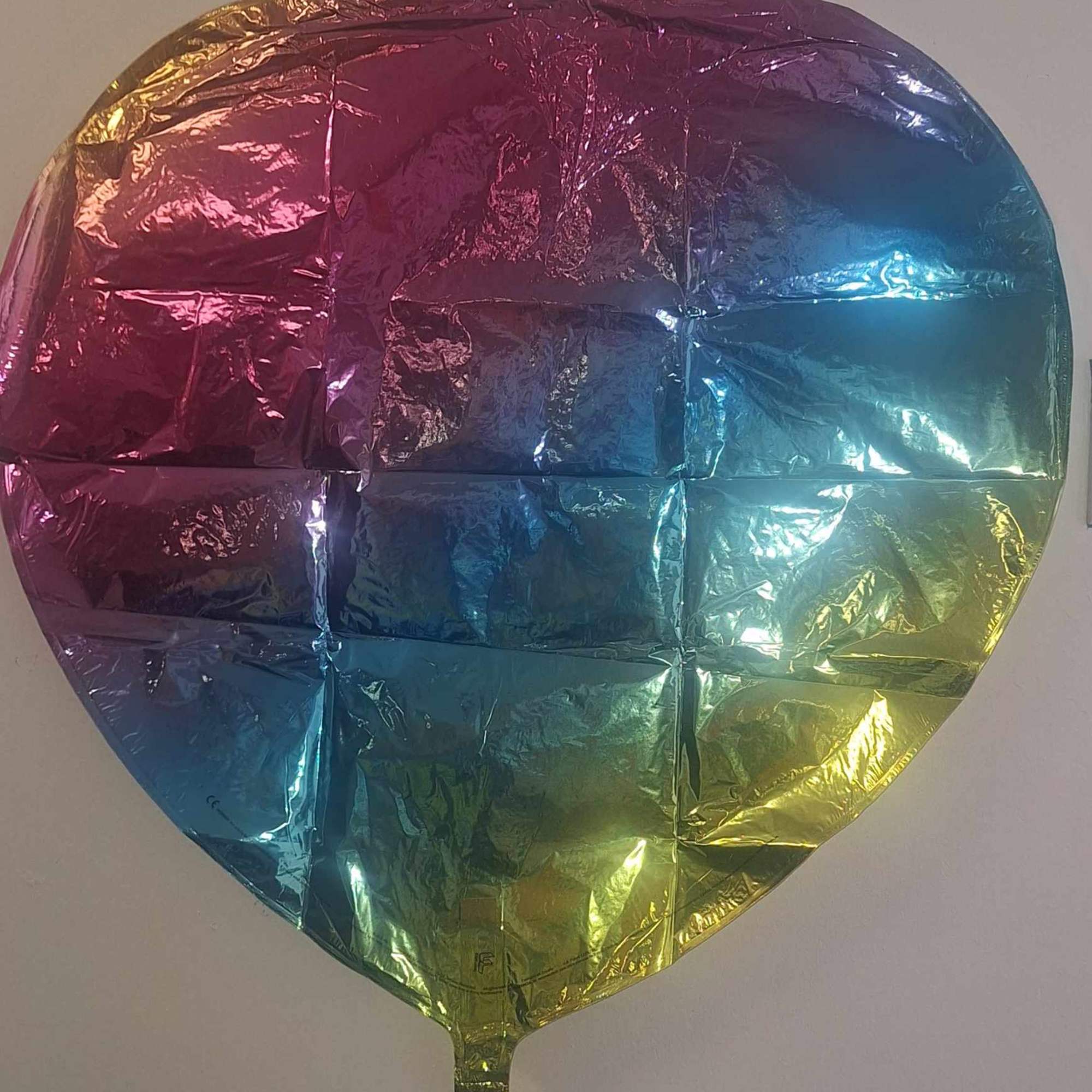 Deflated iridescent heart-shaped foil balloon with pink, blue, and yellow gradient.