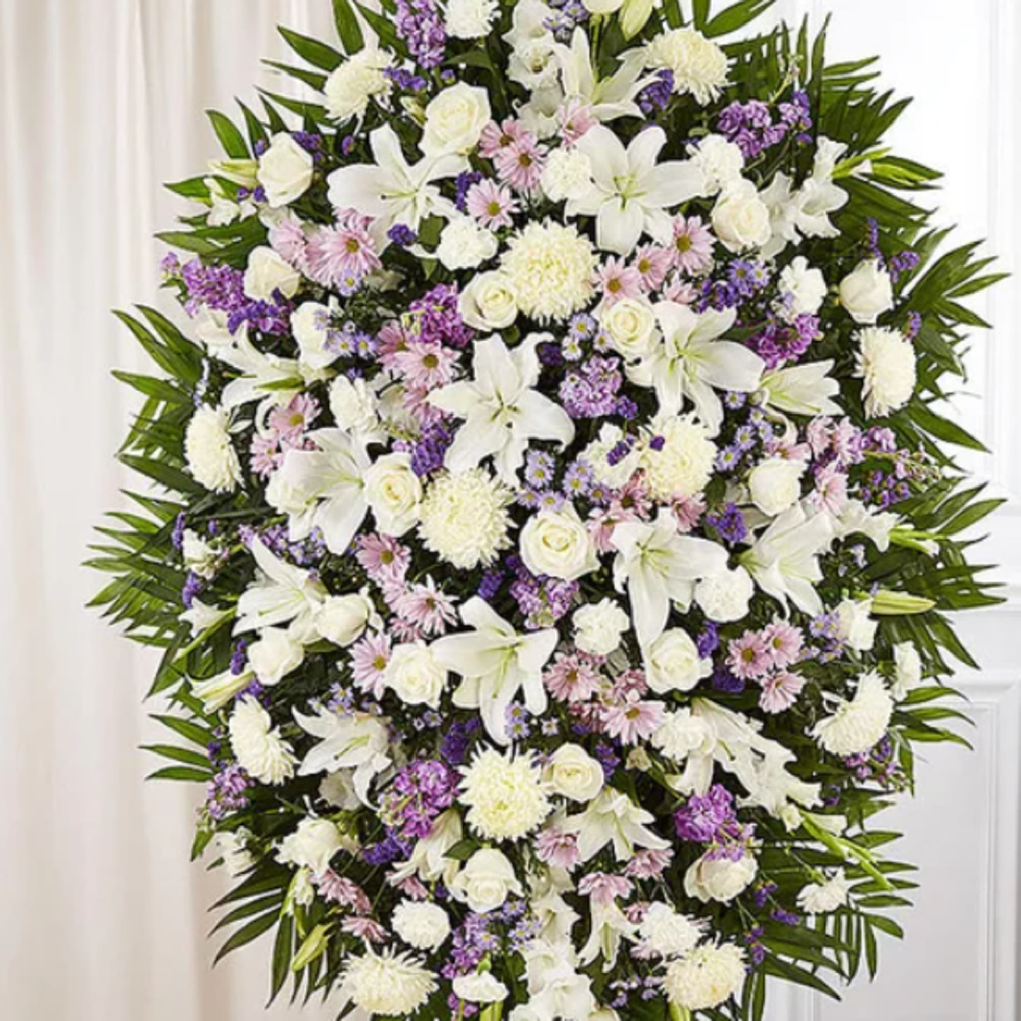 Large white and purple funeral spray with lilies and roses on a stand