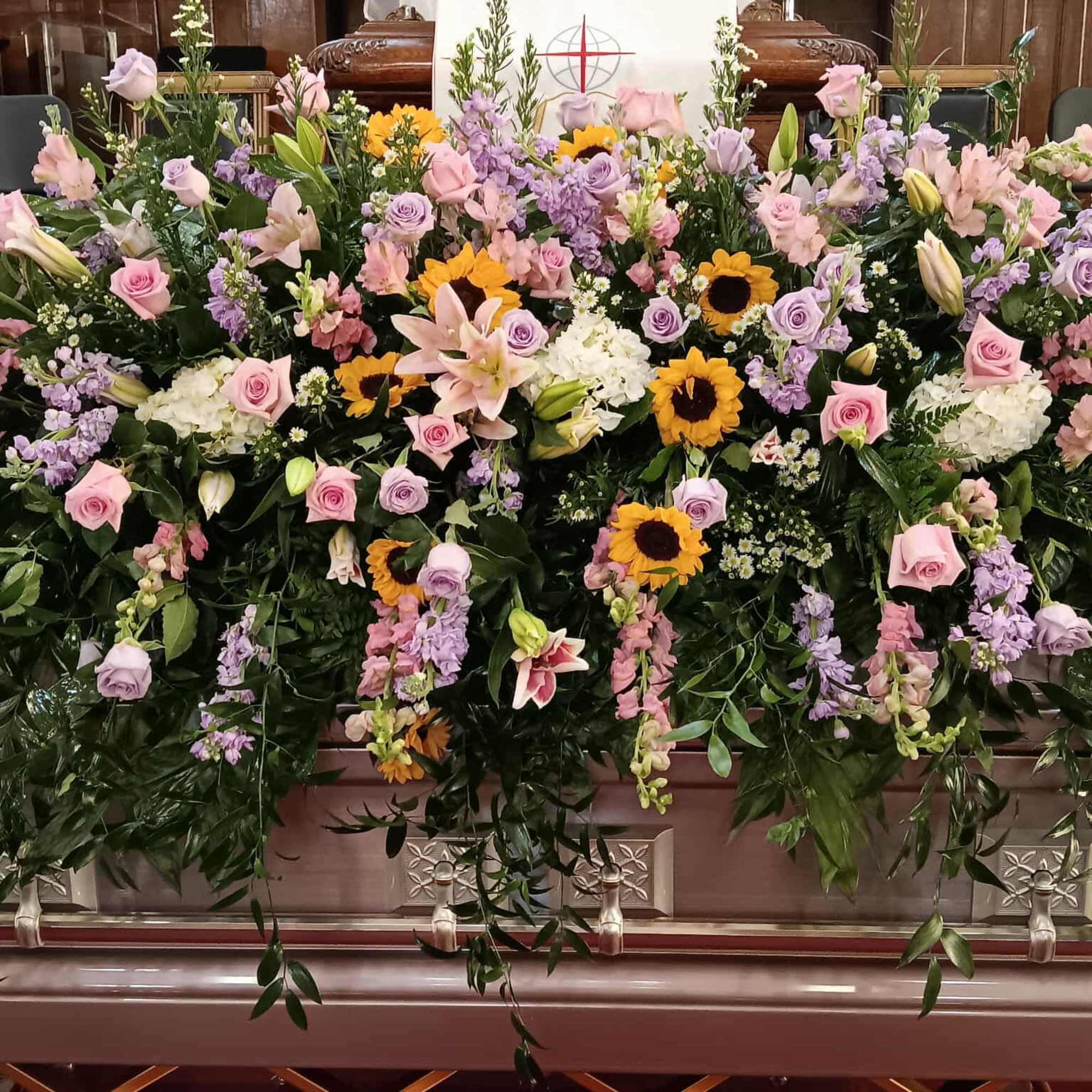 Large pastel floral casket spray with roses, lilies, and sunflowers