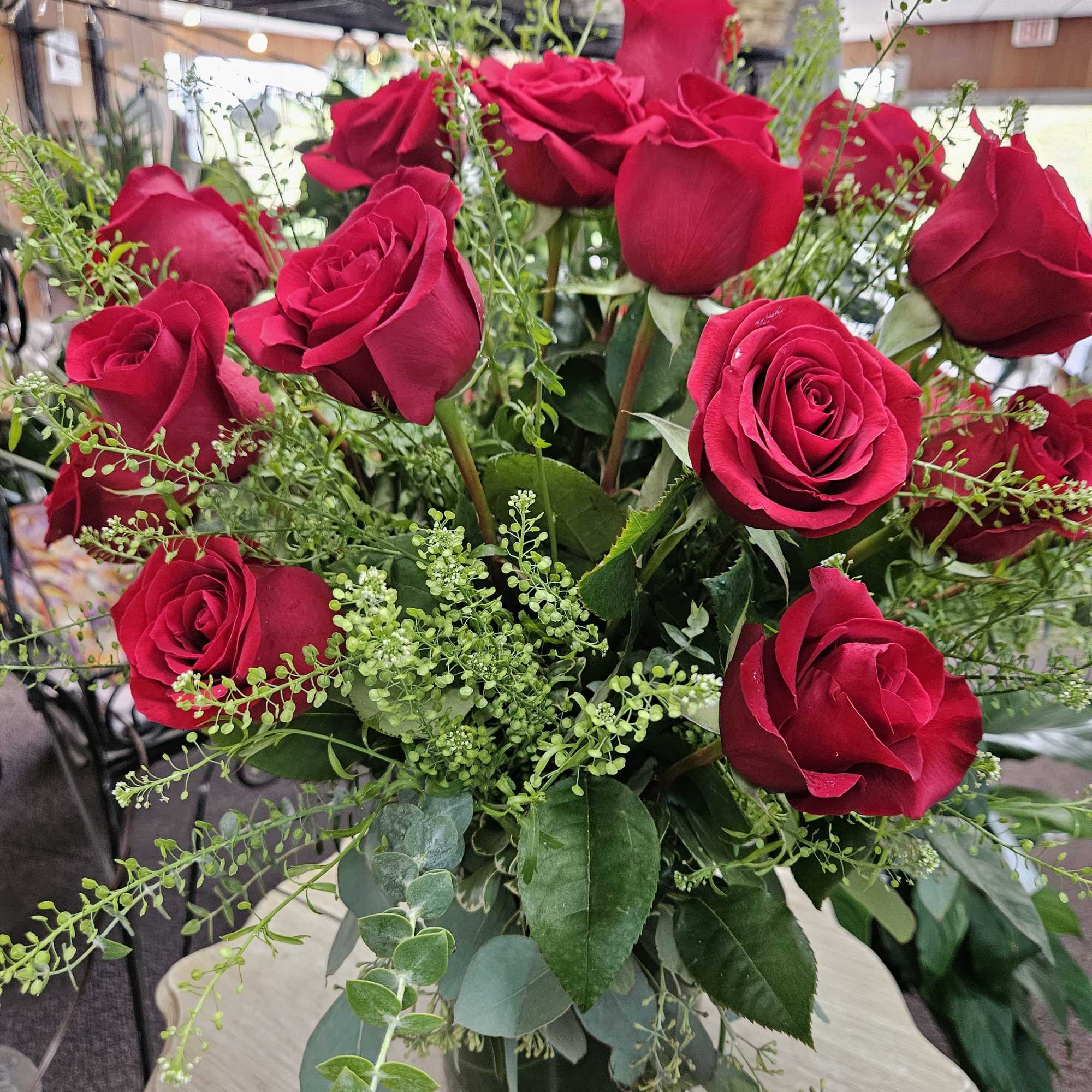 Arrangement of long-stemmed red roses with airy green accents in a clear glass vase on a small table