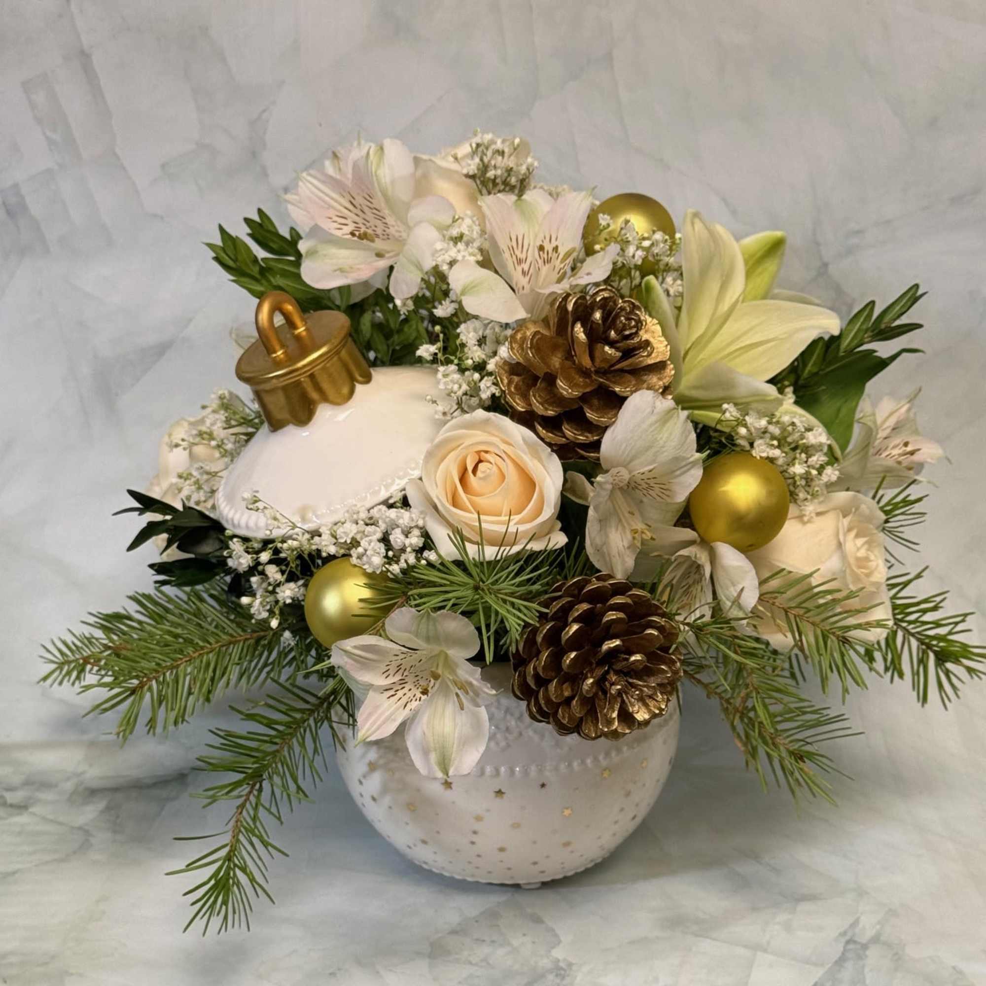 White floral arrangement with lilies, roses, pinecones, and gold ornaments in a ceramic vase