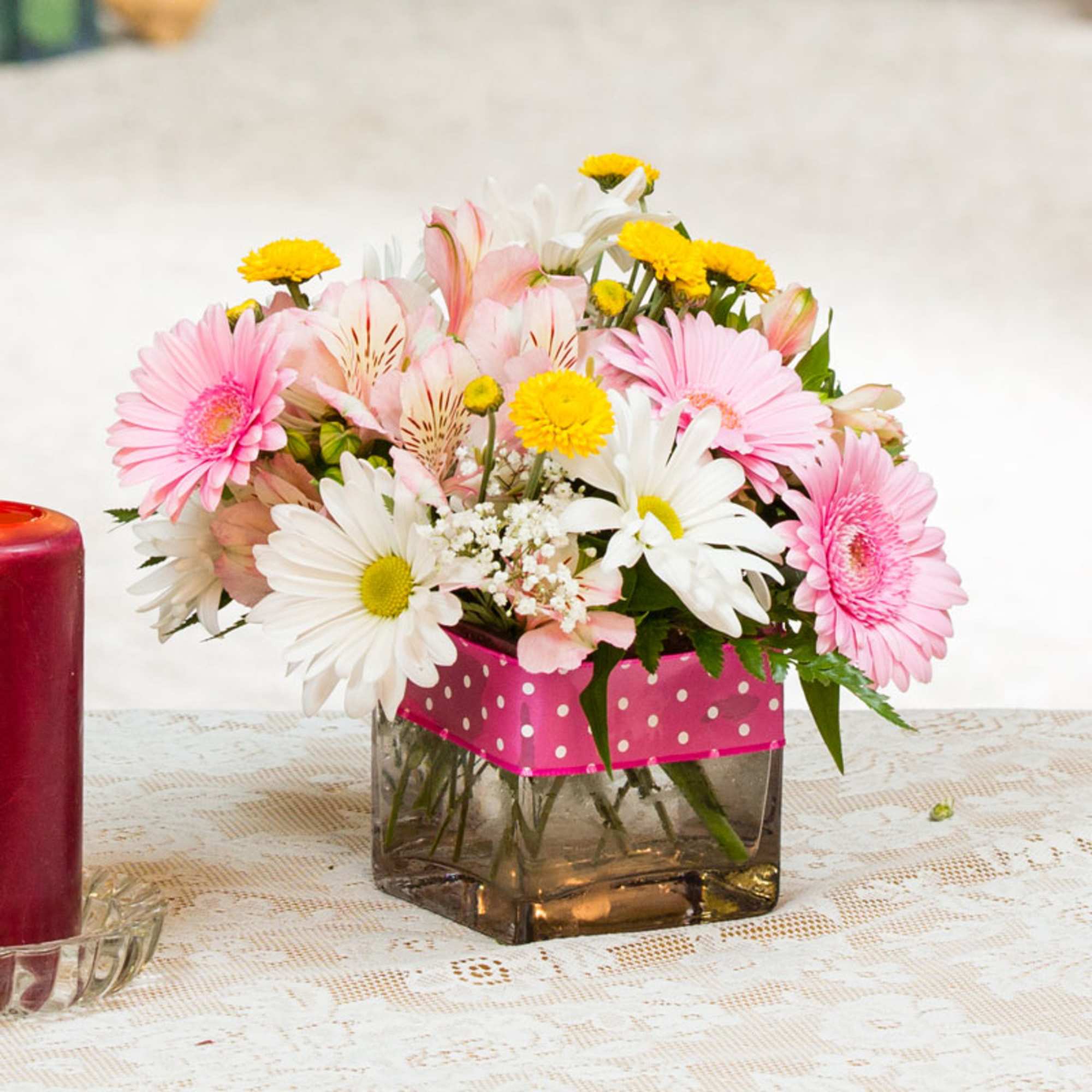 Pink and white mixed flowers in a square glass vase with a polka-dot ribbon