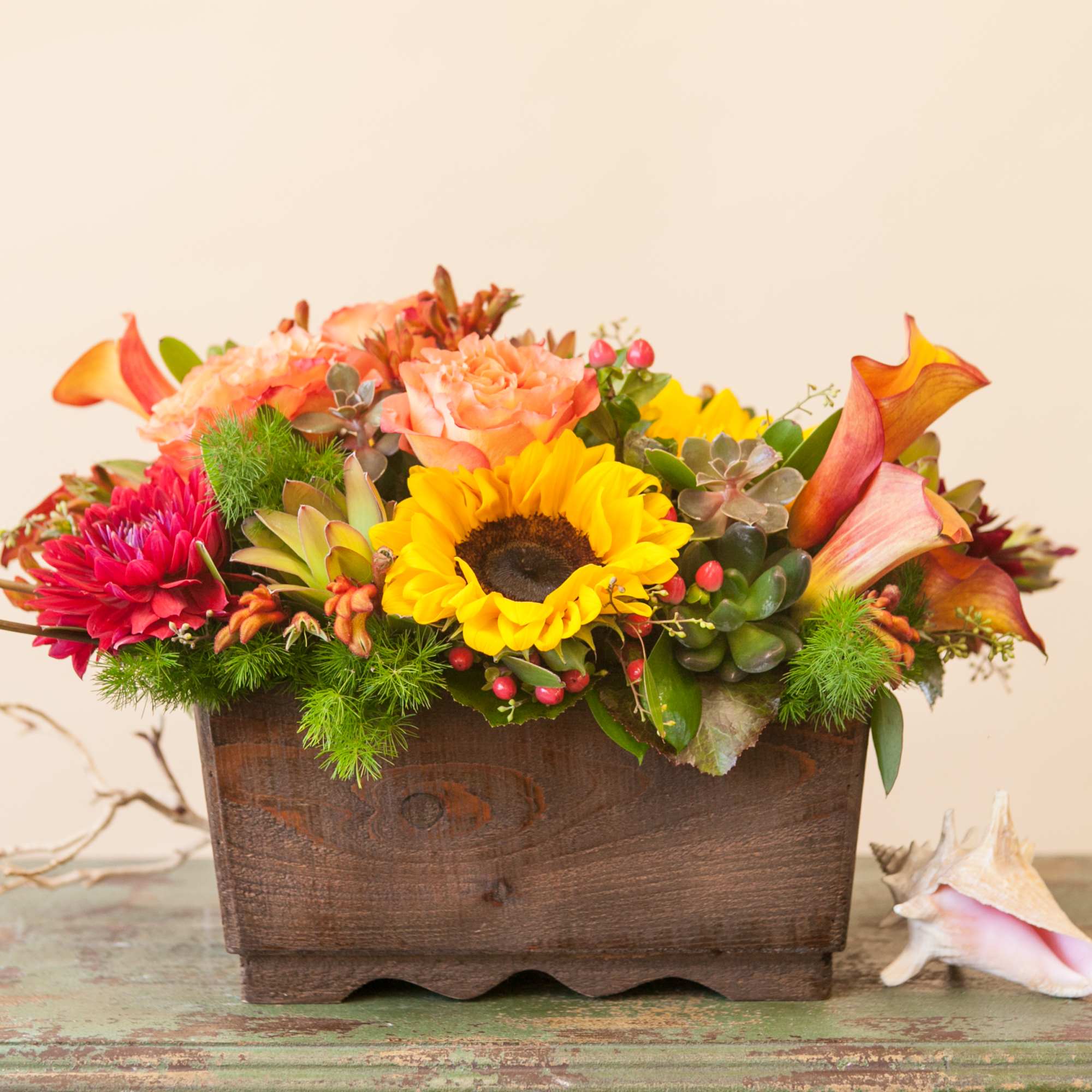 Stunning sunset colored flowers arranged in a large, reusable wooden container- including