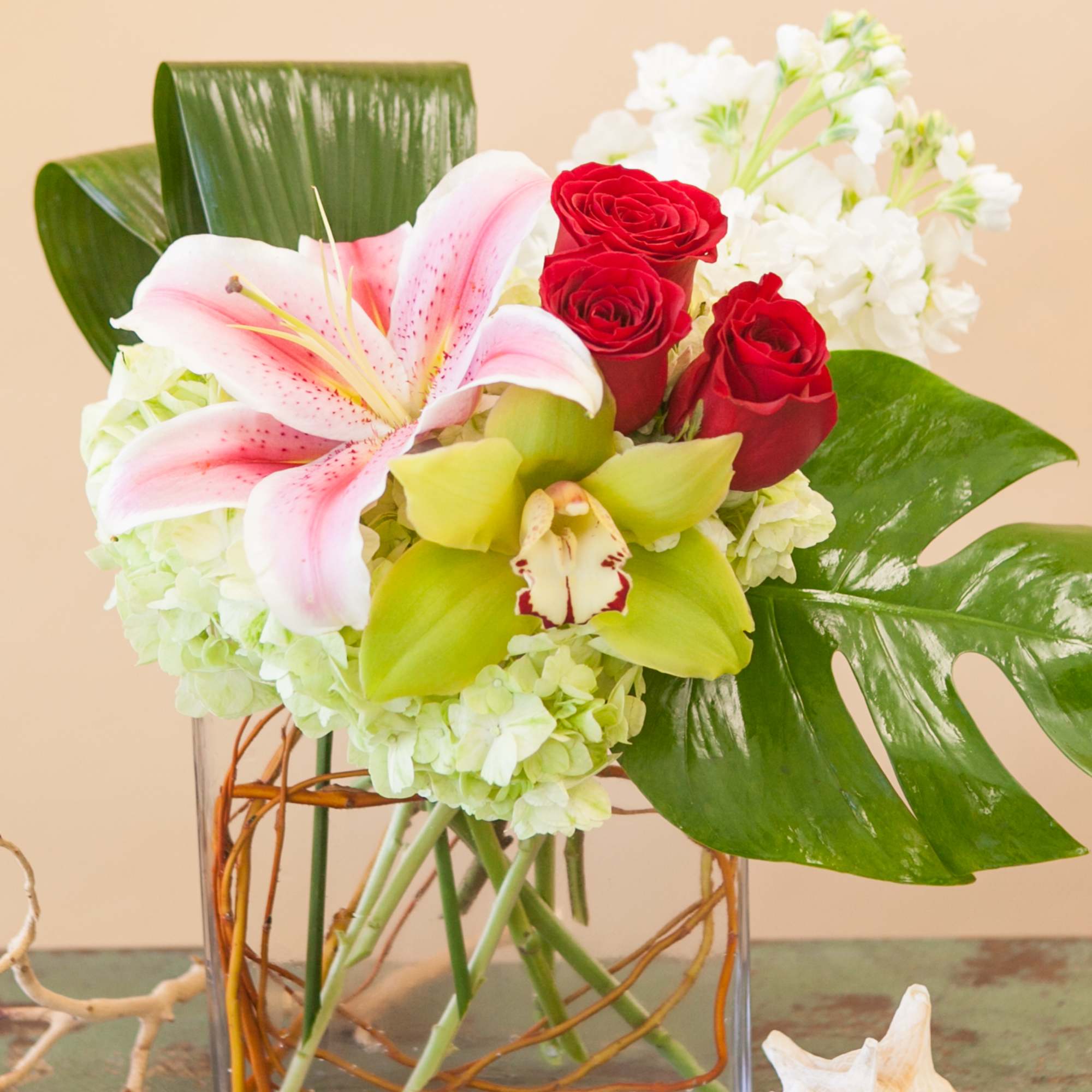 Bouquet of pink lilies, red roses, and white blooms in a glass vase
