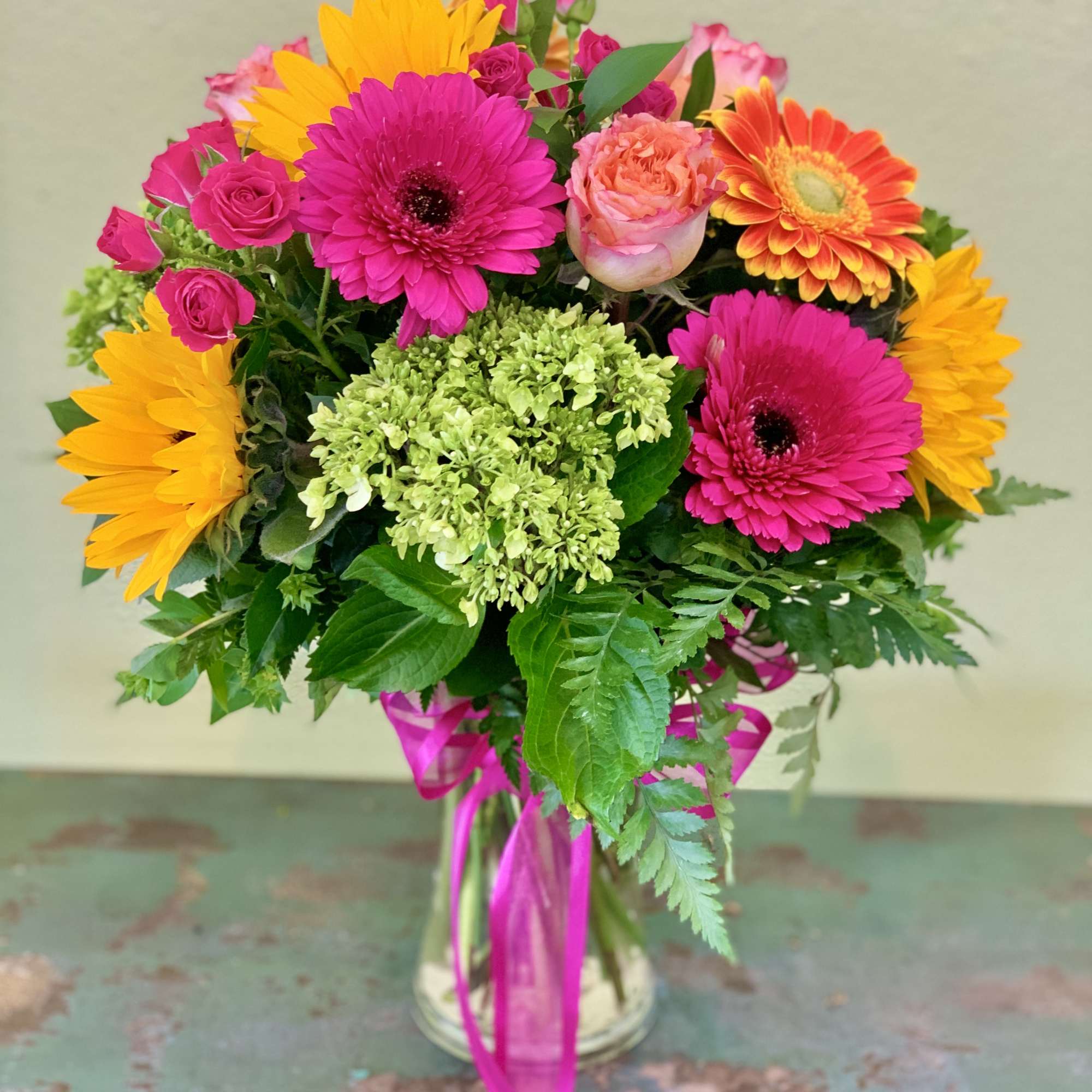 Bouquet of pink and yellow flowers in a glass vase with a pink ribbon